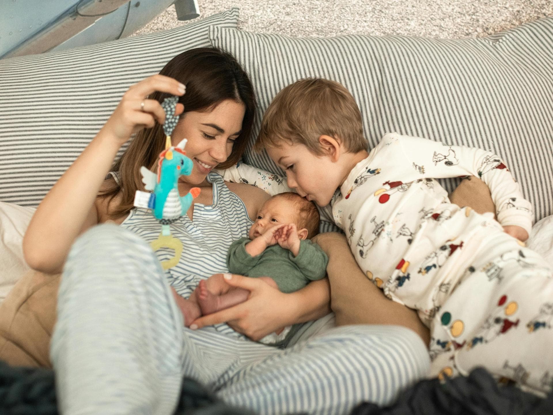 Eine Mutter kuschelt mit ihrem Kleinkind und Baby auf dem Sofa.