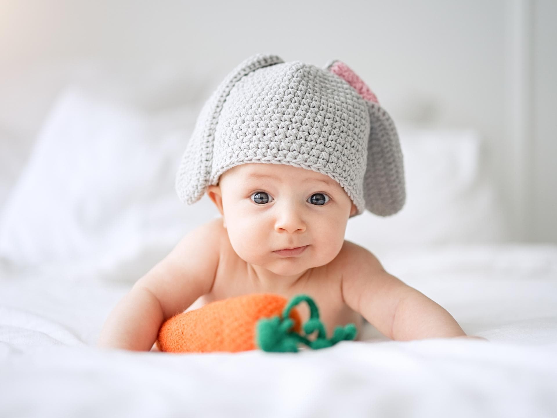 Osternamen für Babys können verschiedene Bedeutungen haben. Baby mit Hasenmütze vor Spielzeug-Möhre.