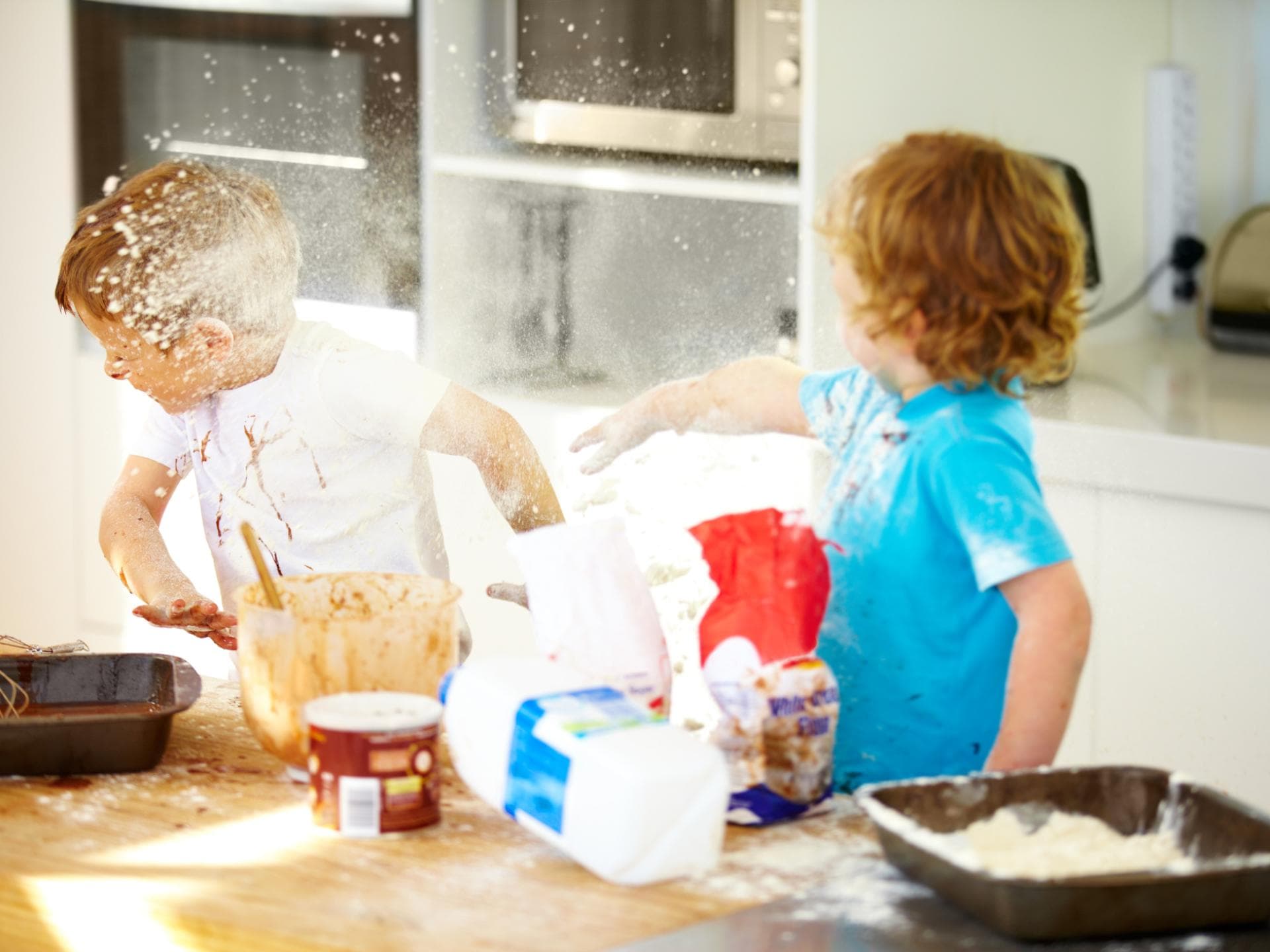 Zwei Kinder streiten beim Backen und bewerfen sich mit Mehl.