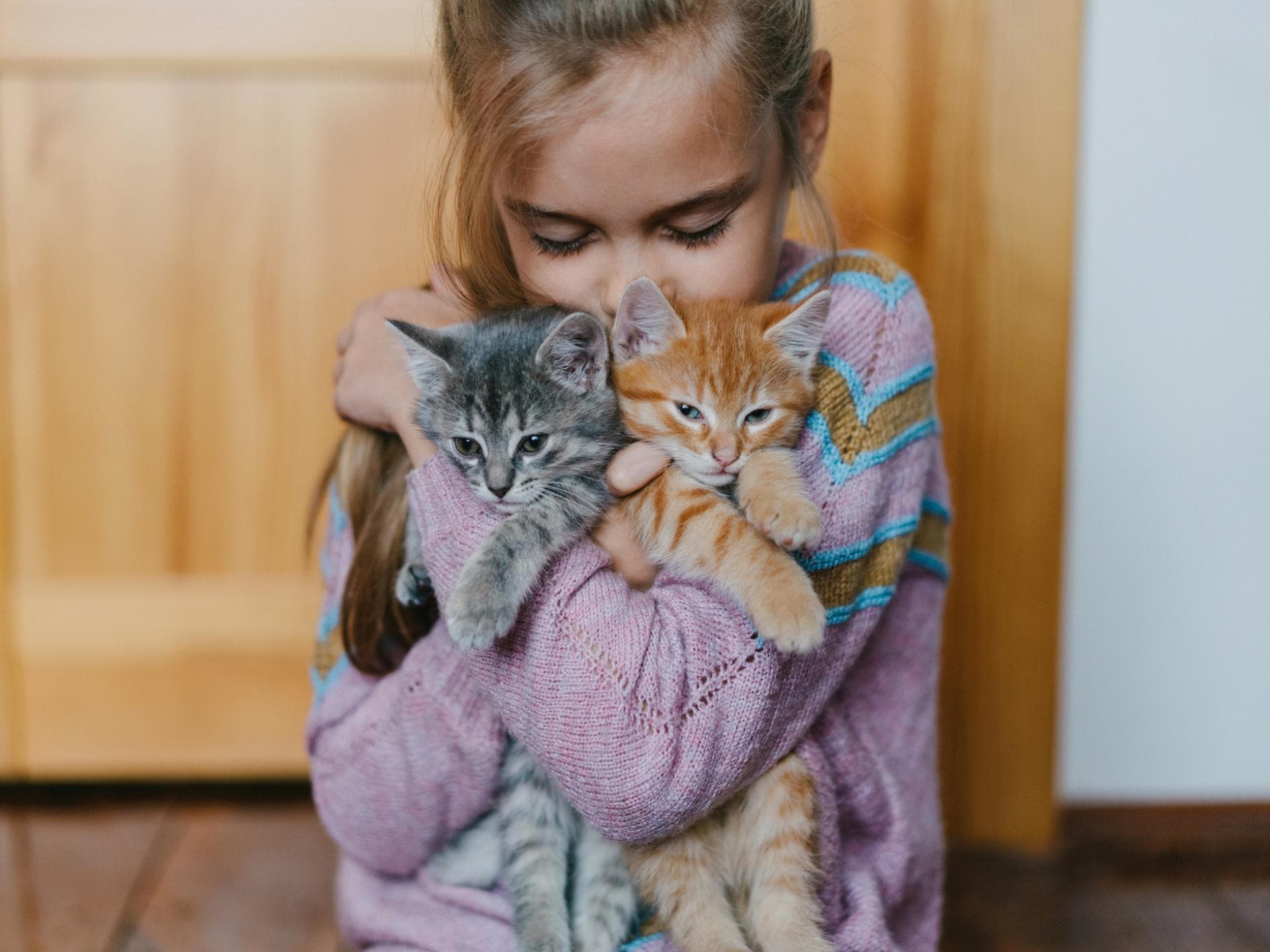 Ein Mädchen kuschelt mit zwei kleinen Katzen. 