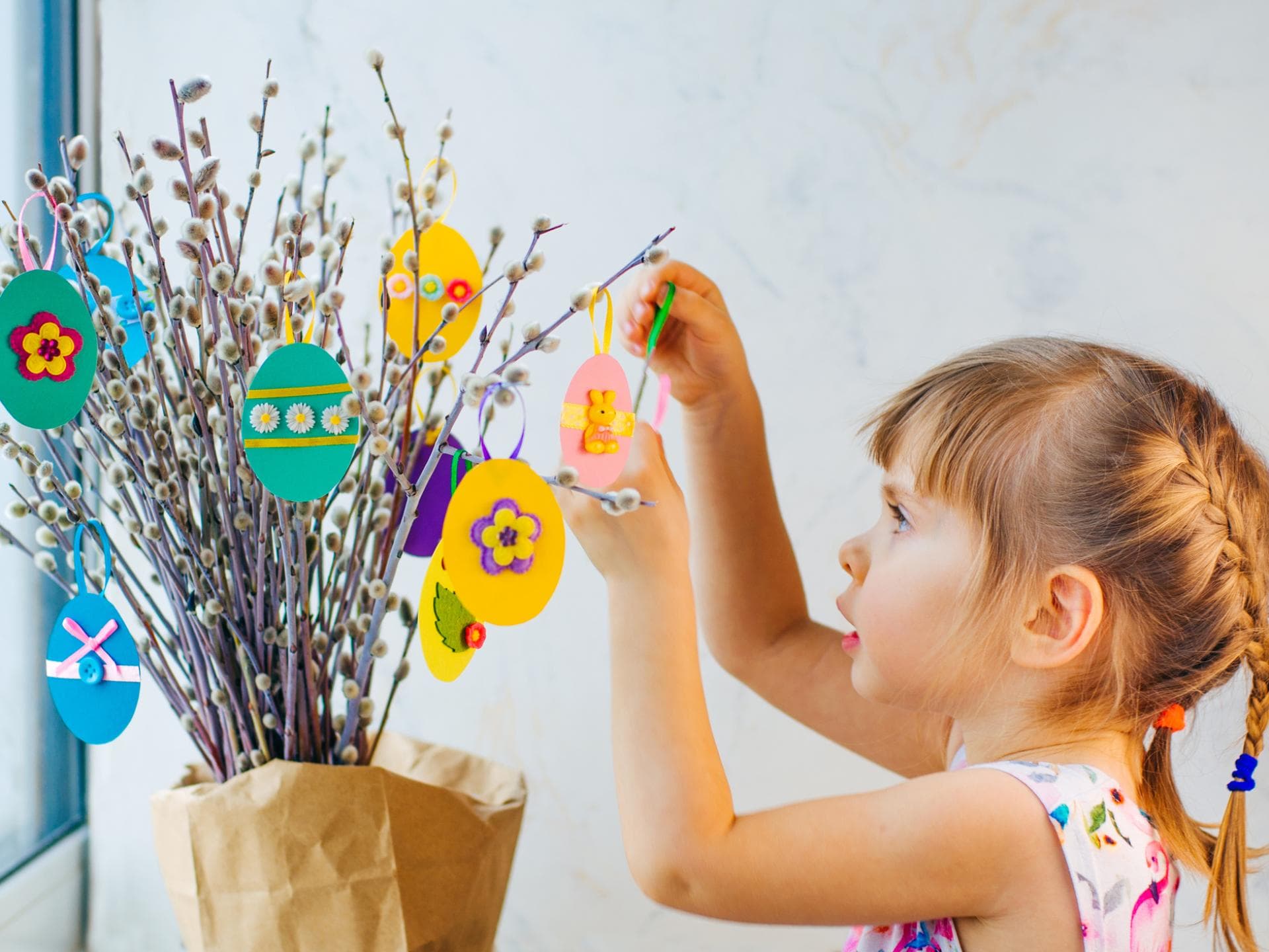Ostereier lassen sich auf vielfältige Art und Weise basteln. Kleines Mädchen hängt selbst gebastelte Ostereier an den Strauch.