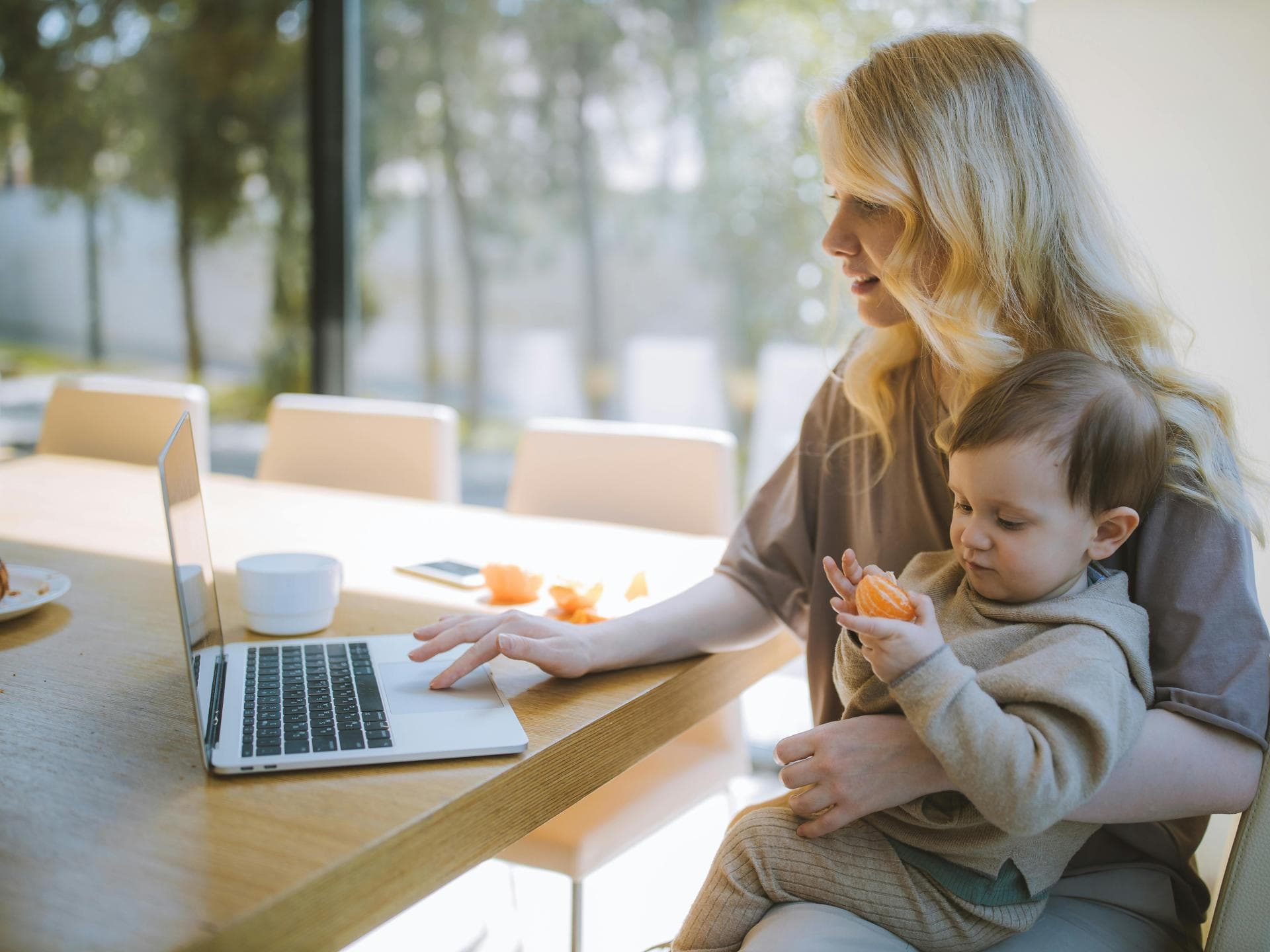 Berufstätige Mütter verfügen oft über starke Soft Skills. Eine Mutter sitzt am Computer und hat ihren kleinen Sohn auf dem Schoß.