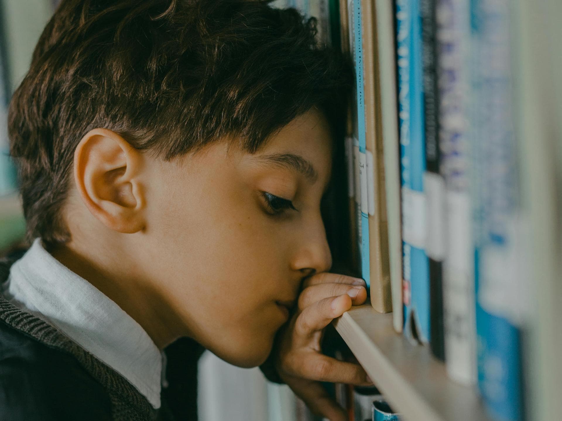 Nachdenklicher Junge lehnt Kopf gegen Bücherregal.