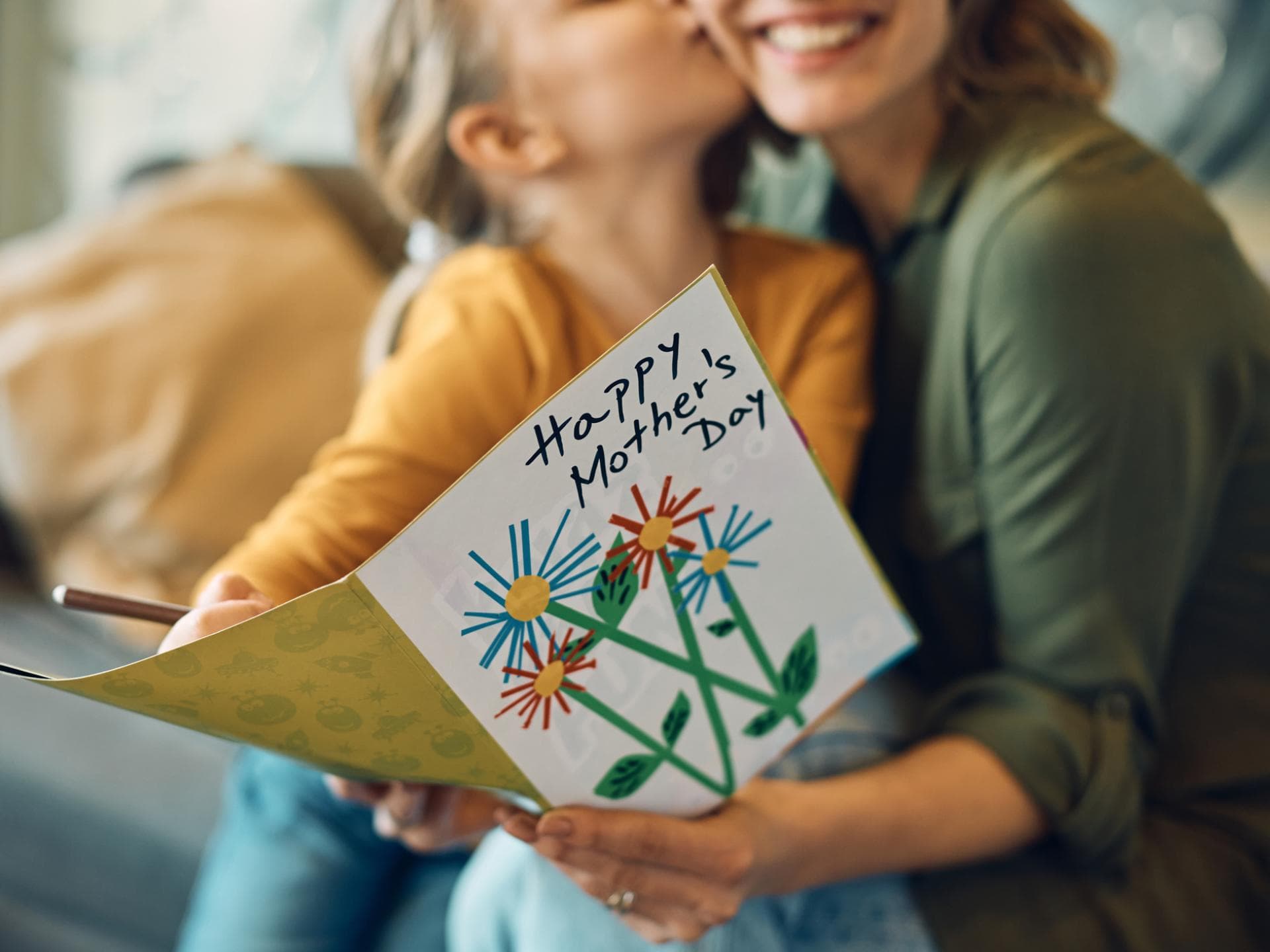Kind küsst Mutter und schenkt ihr eine Karte zum Muttertag.