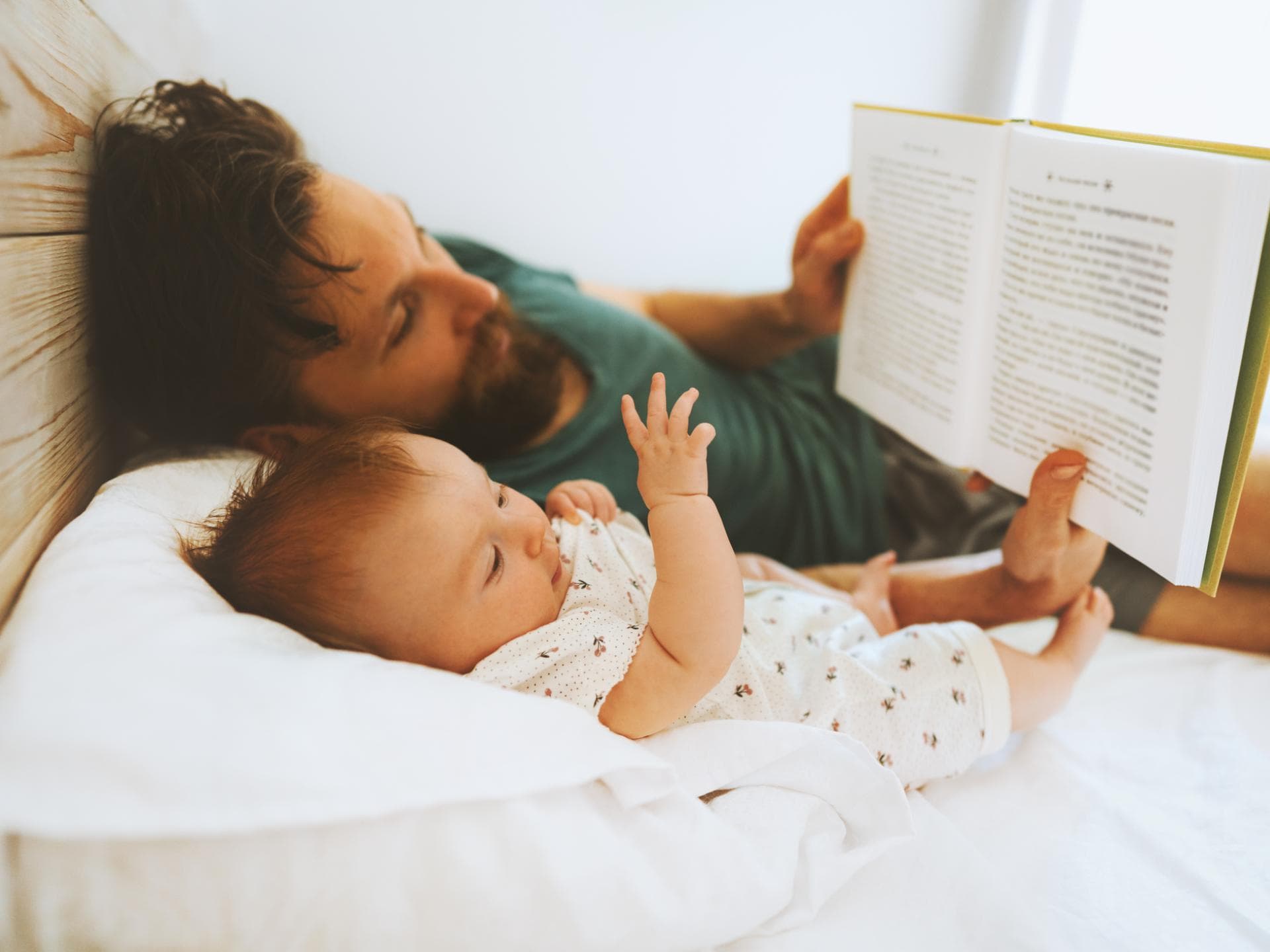 Auch Babys genießen es schon, wenn man ihnen vorliest. Vater liest Baby im Bett vor.