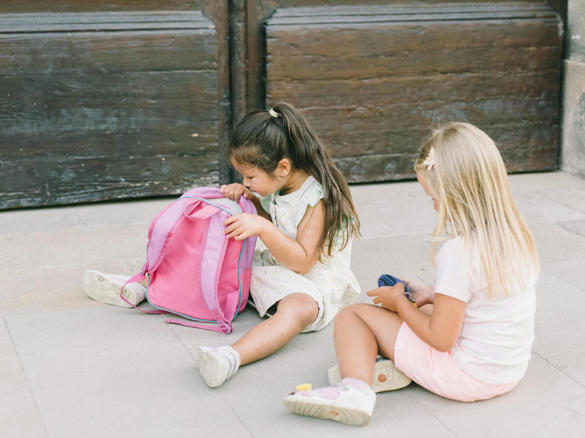 Schulranzen packen will gelernt sein. Zwei Mädchen, das eine schaut in einen Rucksack.