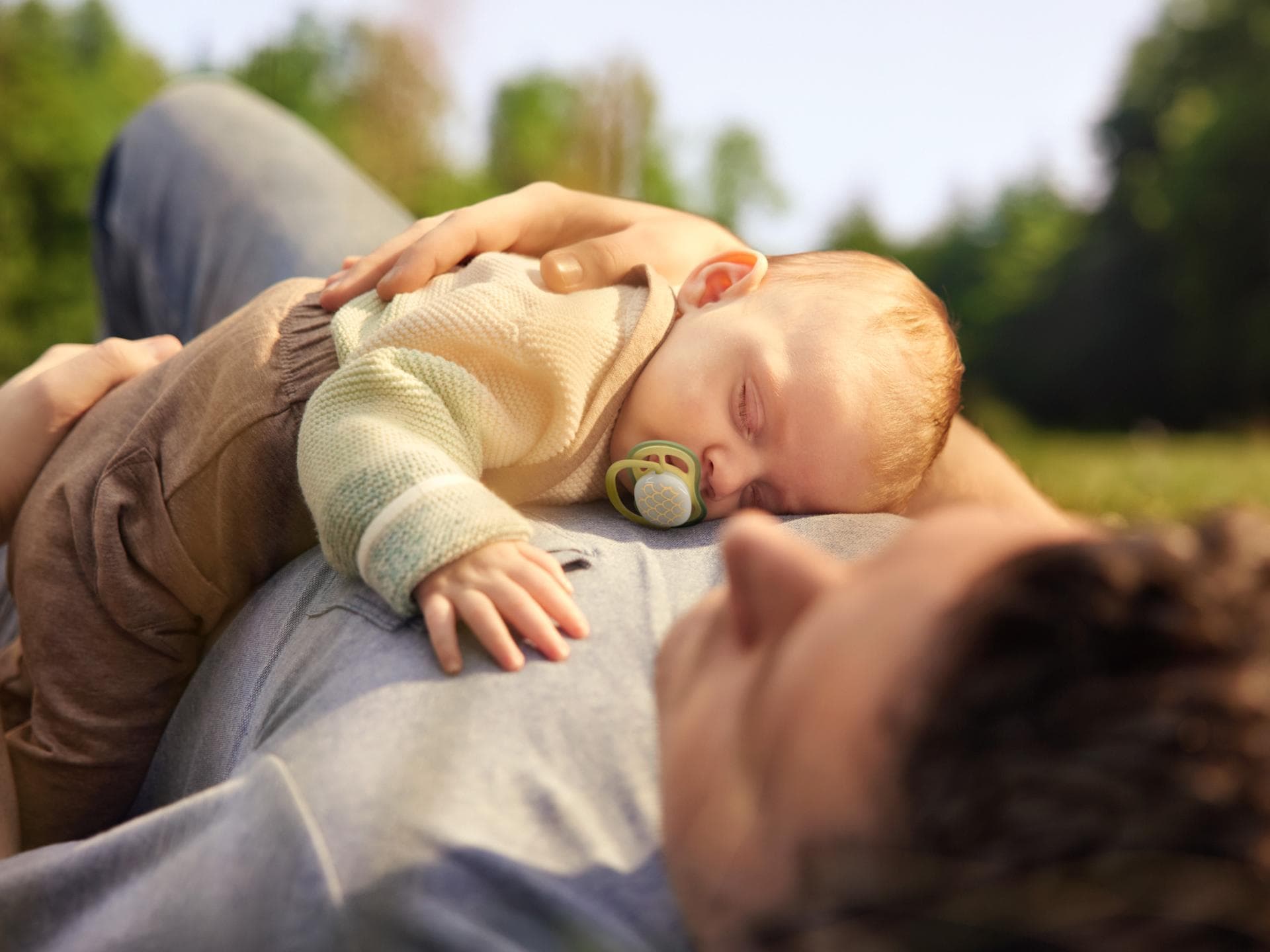 Schlafendes Baby mit Schnuller liegt auf Papas Bauch.