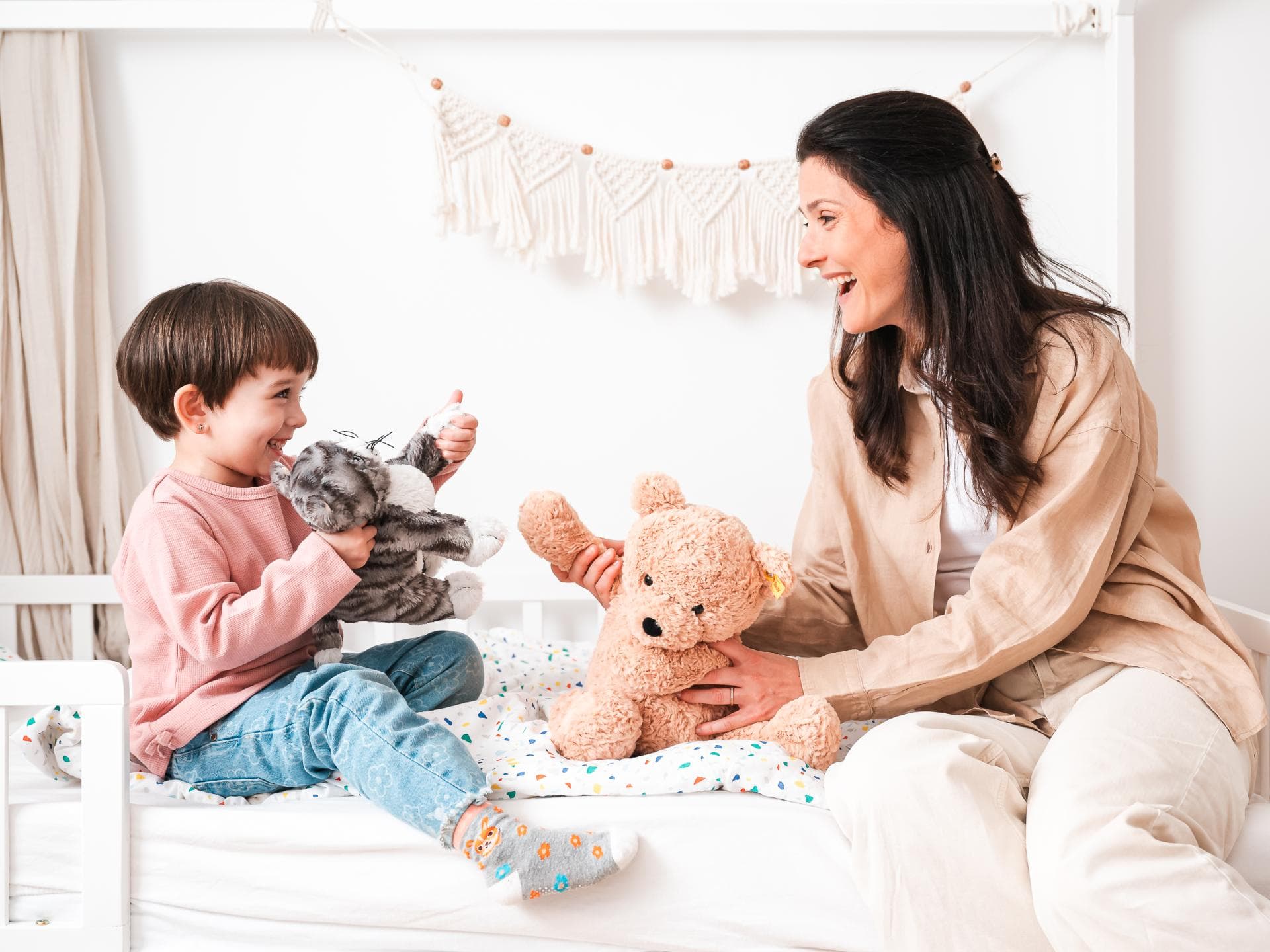Mutter und Kind spielen auf Bett mit Kuscheltieren.