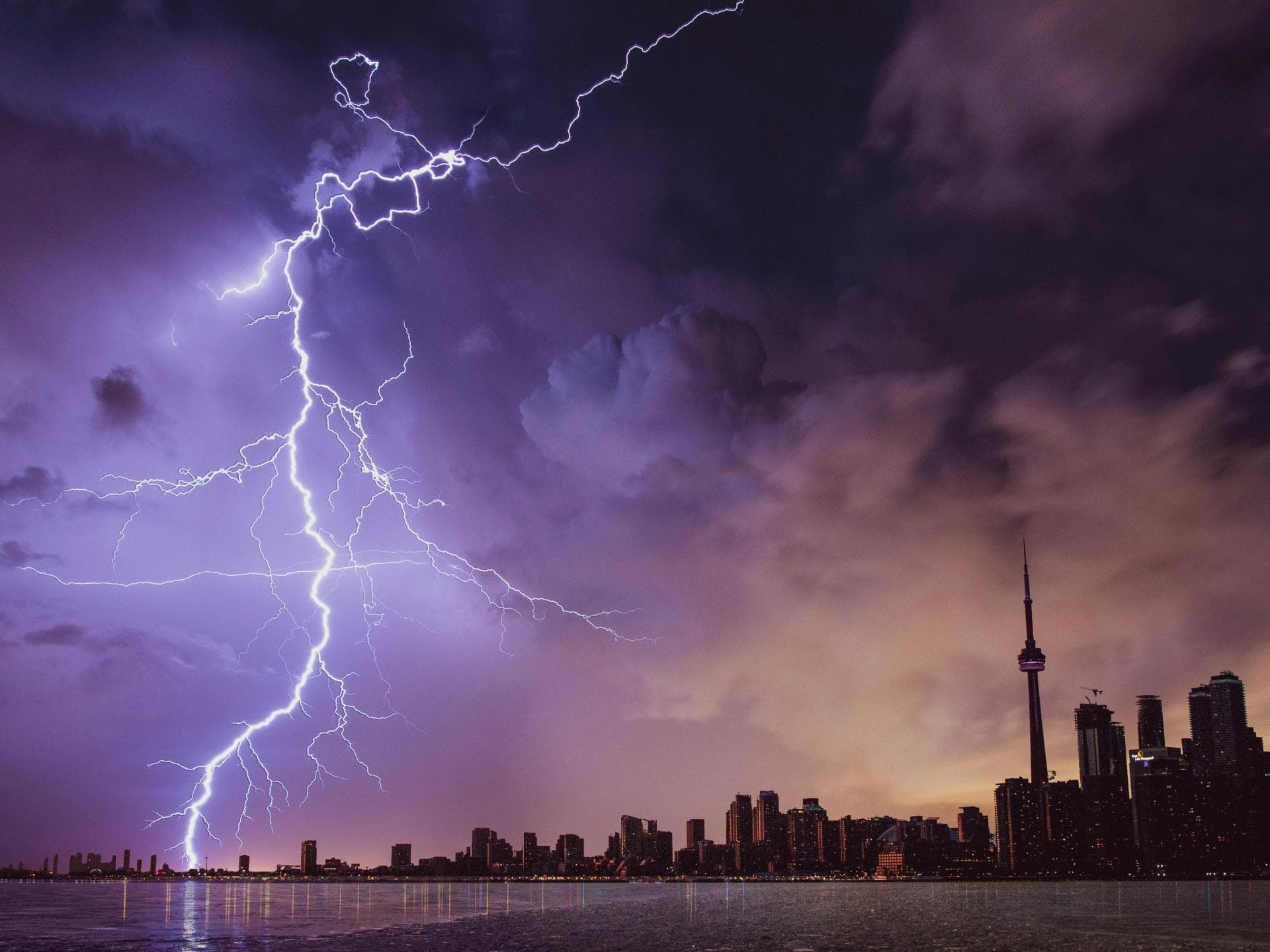 Bei Gewitter sollte man über das richtige Verhalten Bescheid wissen. Ein Blitz schlägt nahe einer Stadt ein.