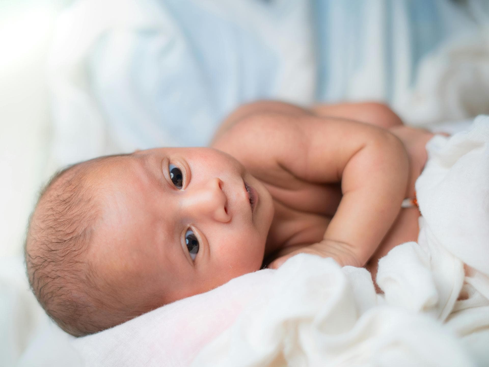 Die Babyhaut braucht ganz besondere Pflege. Baby liegt auf der Seite.