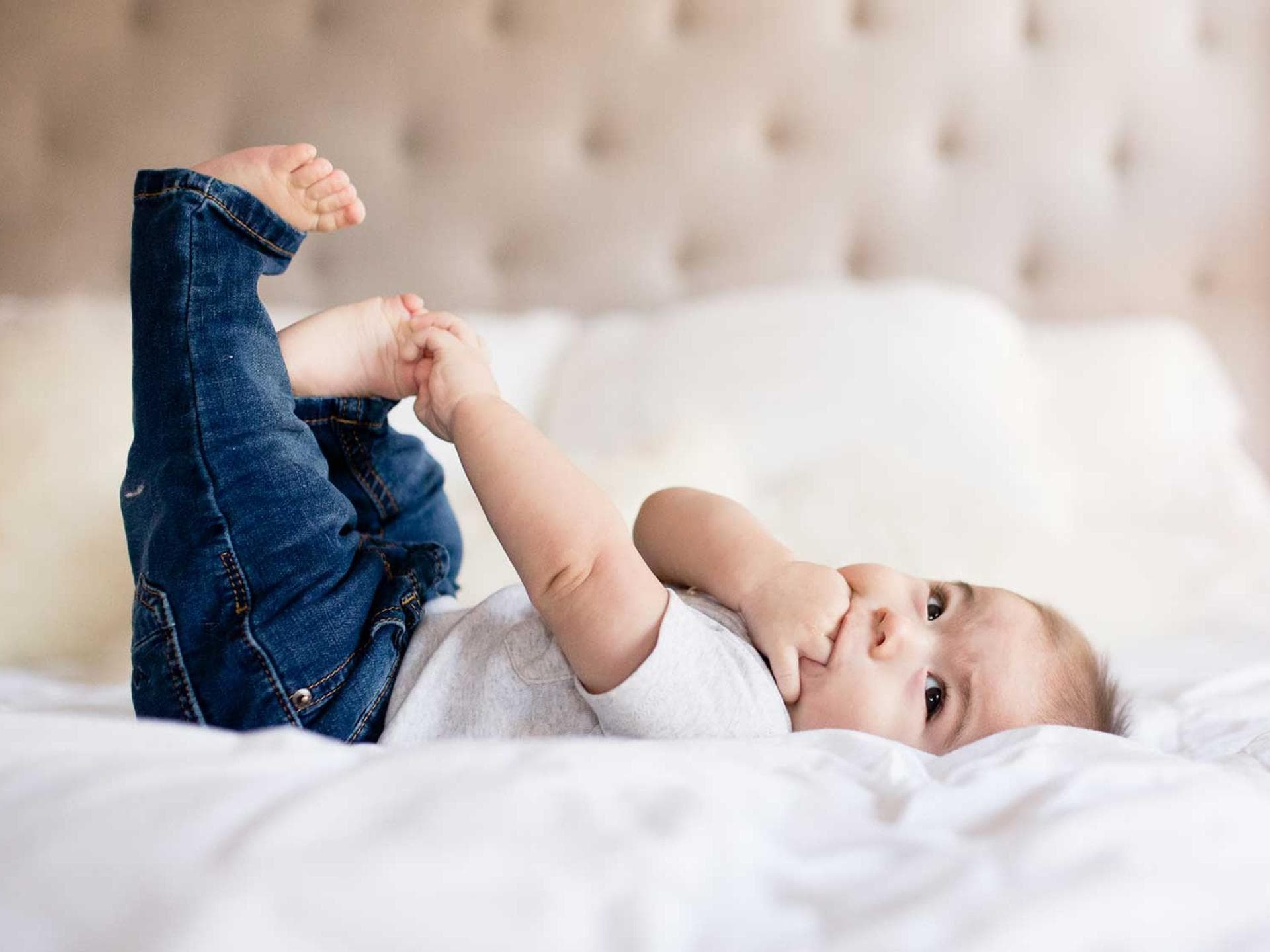 Ein kleines Baby mit Jeans liegt auf einem Bett. 