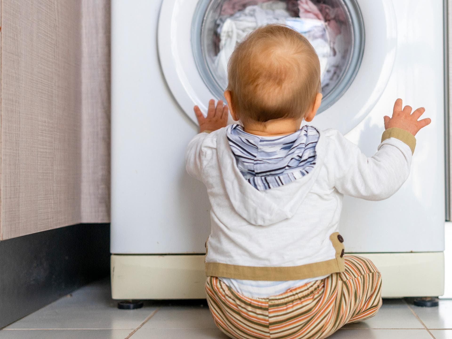 Baby sitzt vor der Waschmaschine und schaut hinein.