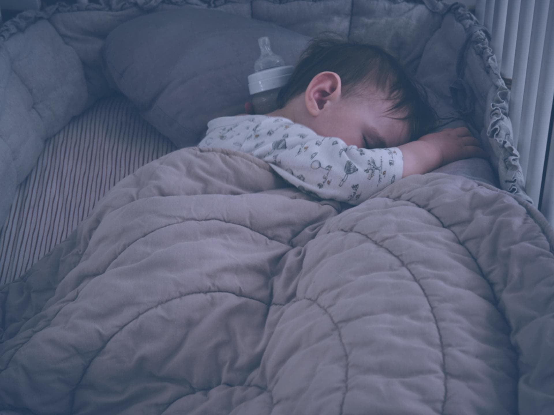 Baby im Bett mit Nestchen und Decke.