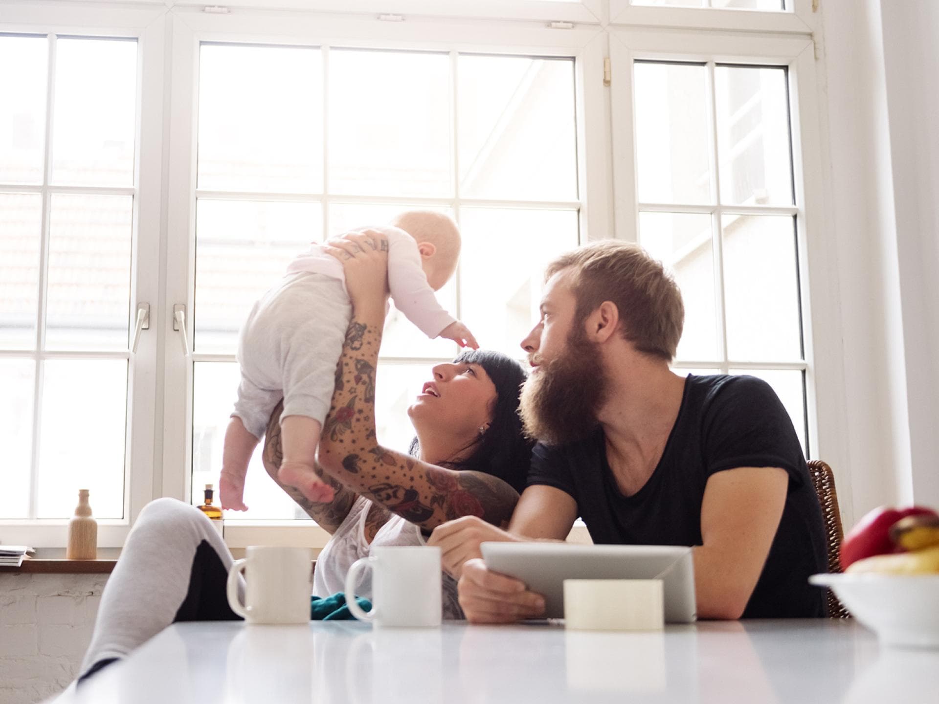 Nicht nur Berlins Bewohner sind besonders kreativ, auch viele Babynamen sind einzigartig! Eine Mutter hält ihr Baby in die Luft, der Vater sitzt daneben und schaut zu.