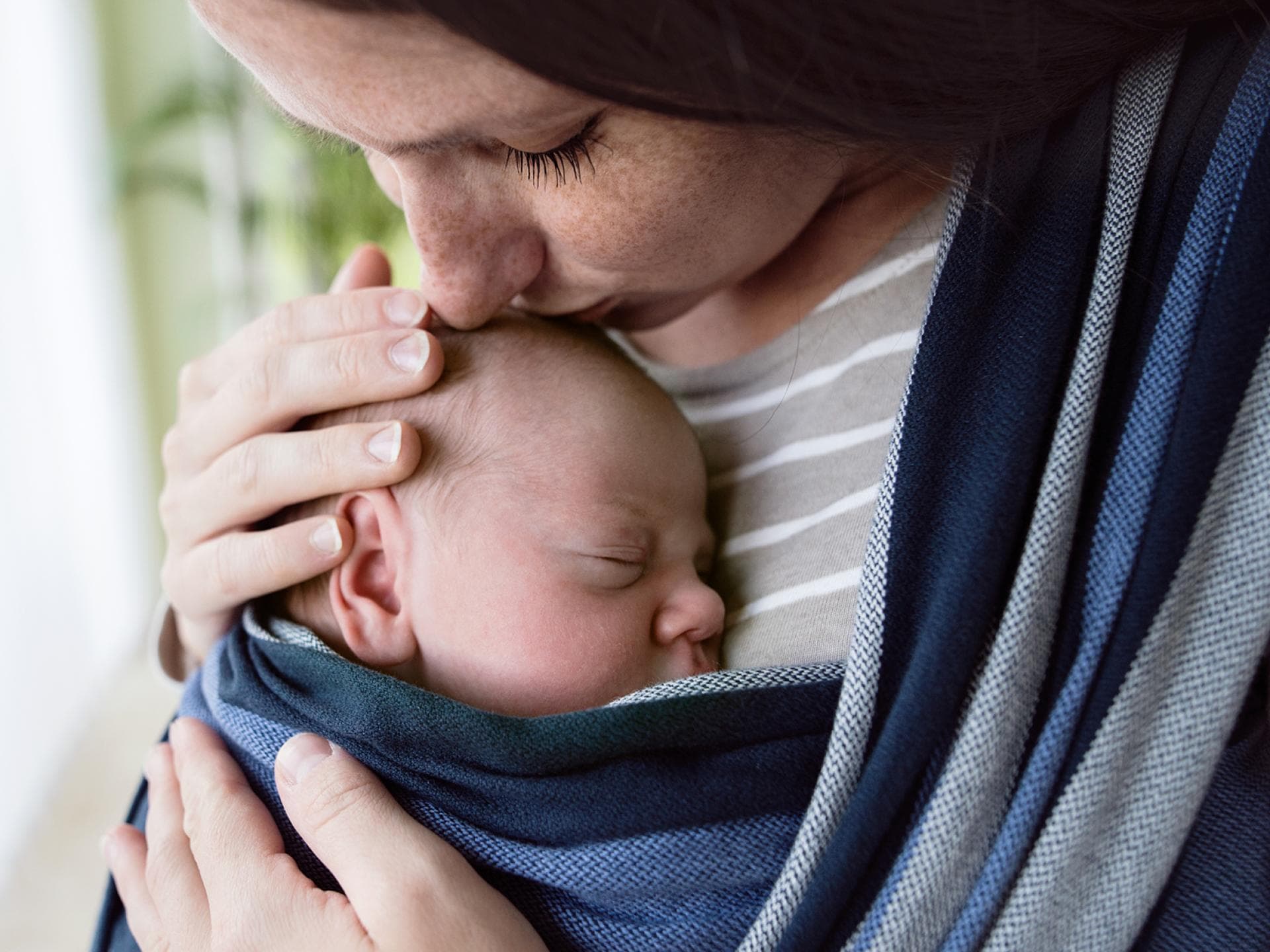 Mutter hat kleines Baby im Tragetuch und kuschelt zärtlich mit ihm.