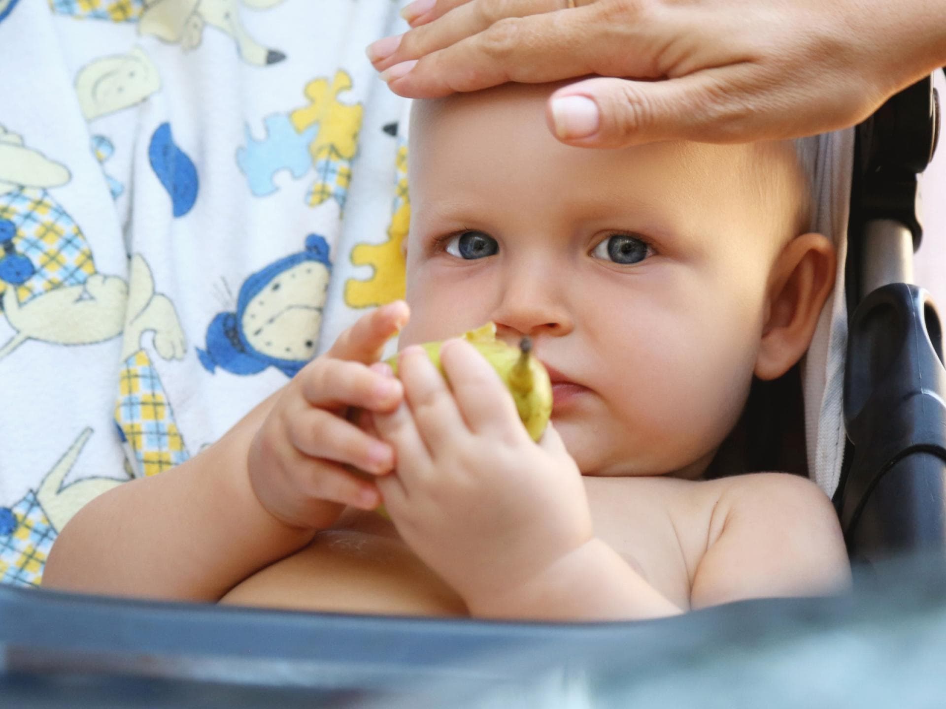Eltern sollten im Sommer regelmäßig checken, ob ihrem Baby zu warm ist. Eine Mutter fühlt die Stirn ihres Babys.