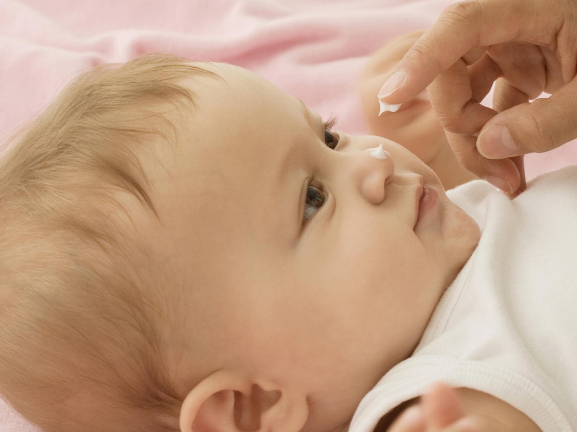 Schadet Eincremen Babys Haut? Oder tut es ihr gut? Baby bekommt Creme auf die Nase getupft.