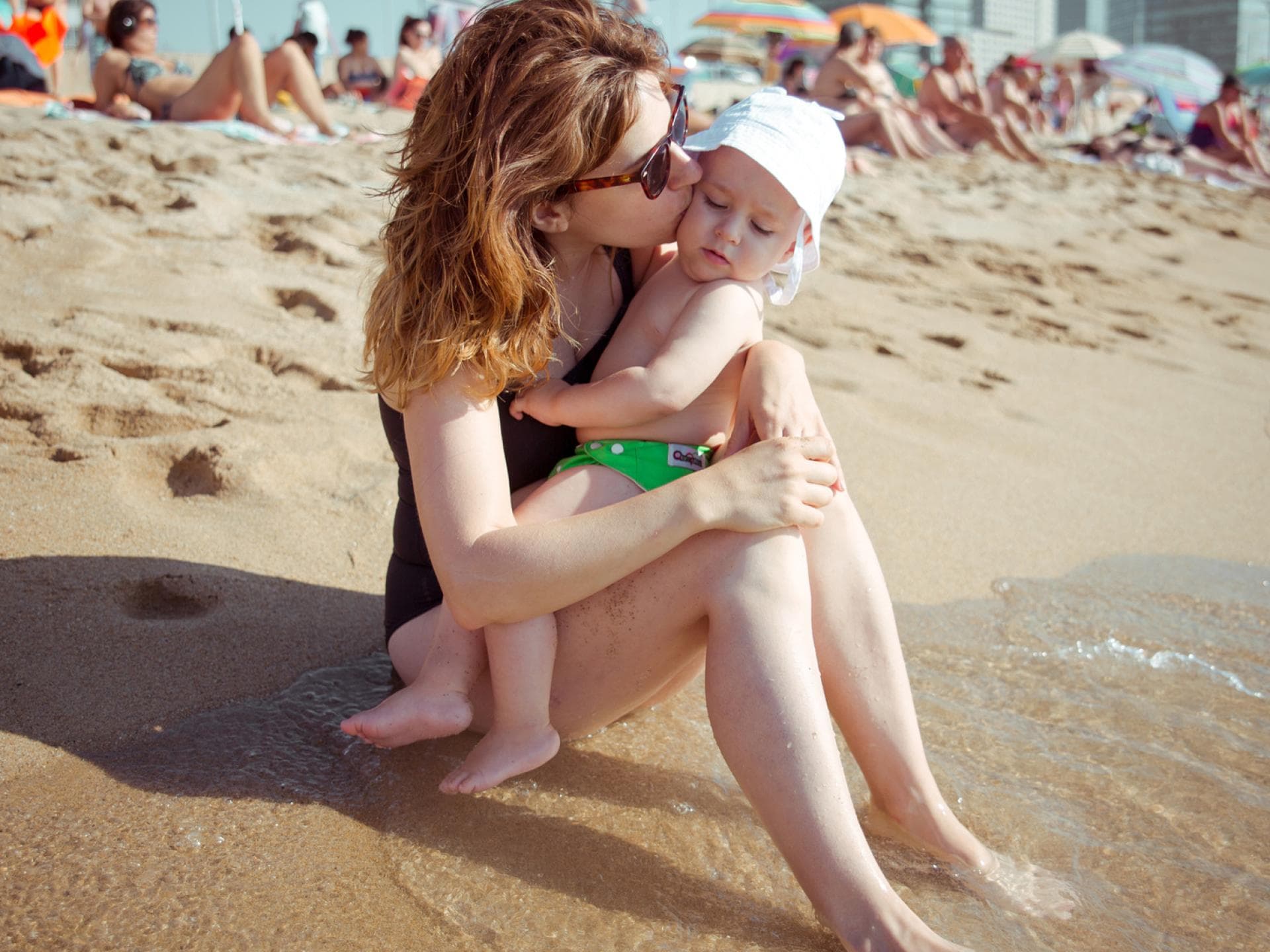 Kann Kokosöl bei Babys wirklich als Sonnenschutz eingesetzt werden?  Eine Mama und ihr Baby kuscheln am Strand.