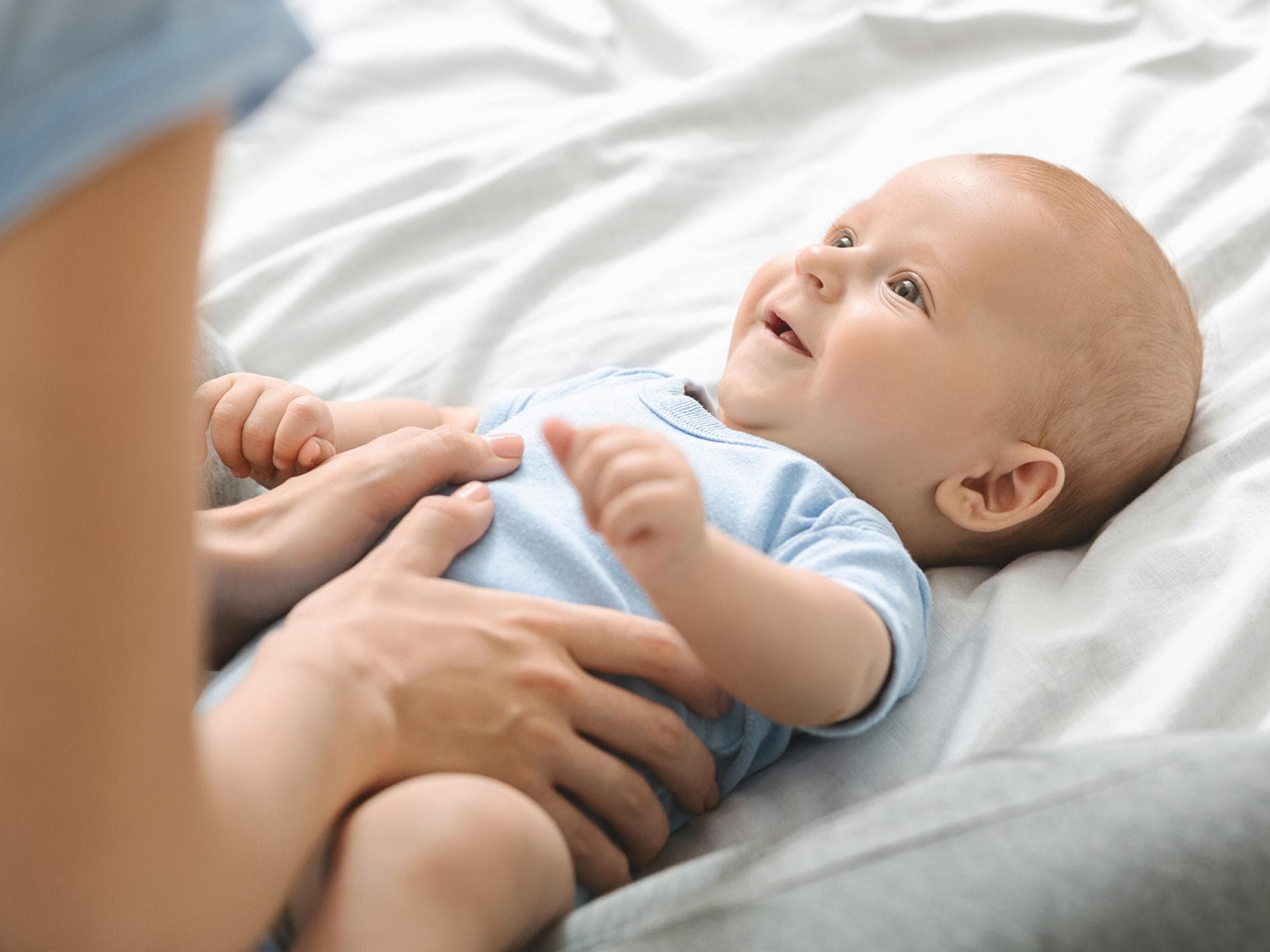 Viele Babys leiden anfänglich unter Bauchweh. Mama hält Bäuchlein eines fröhlichen Babys.
