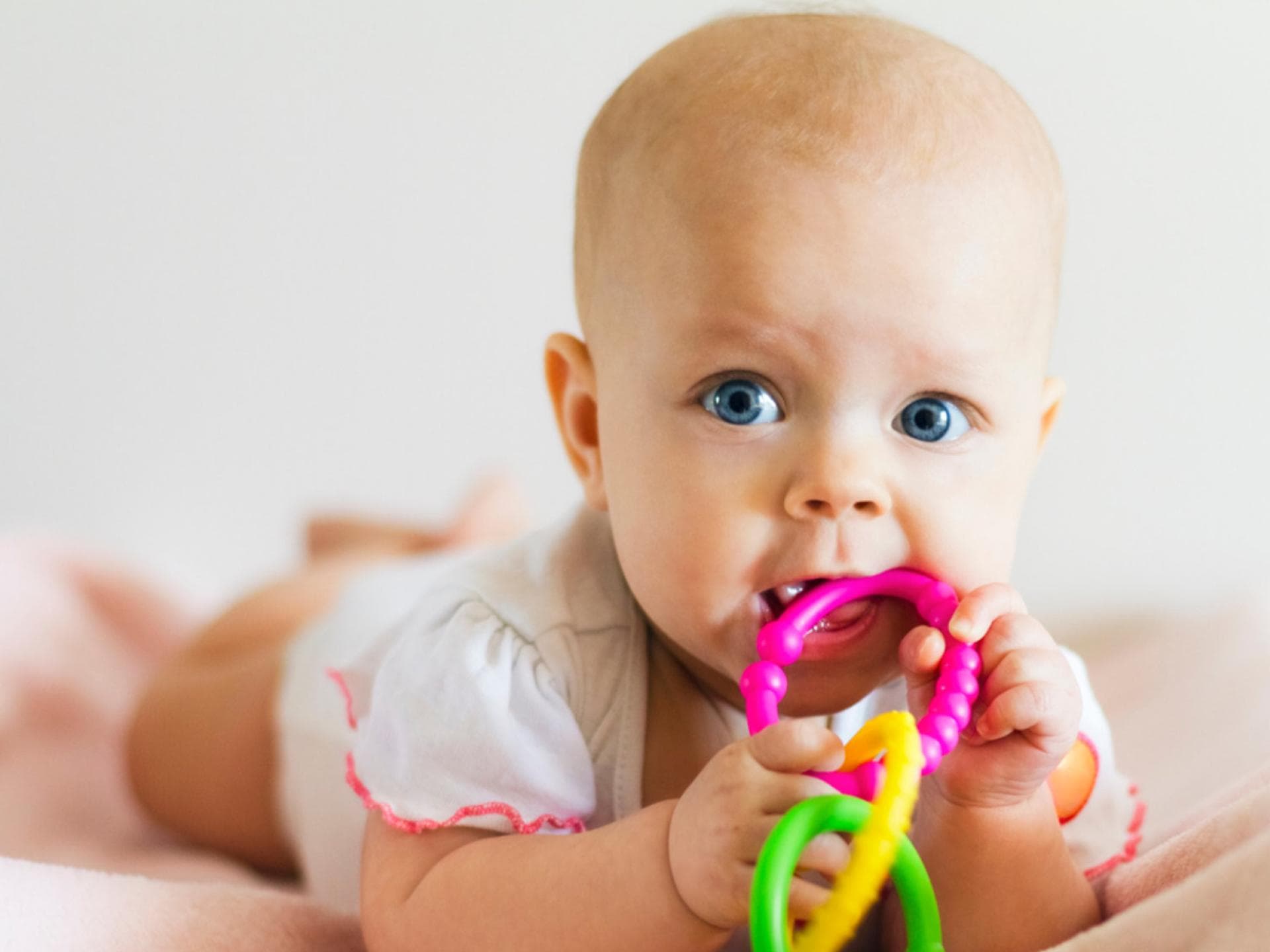 Zahnen kann für Babys mitunter ganz schön unangenehm sein. Gekühlte Schnuller oder Ringe können helfen. Baby liegt auf dem Bauch und kaum am Beißring.