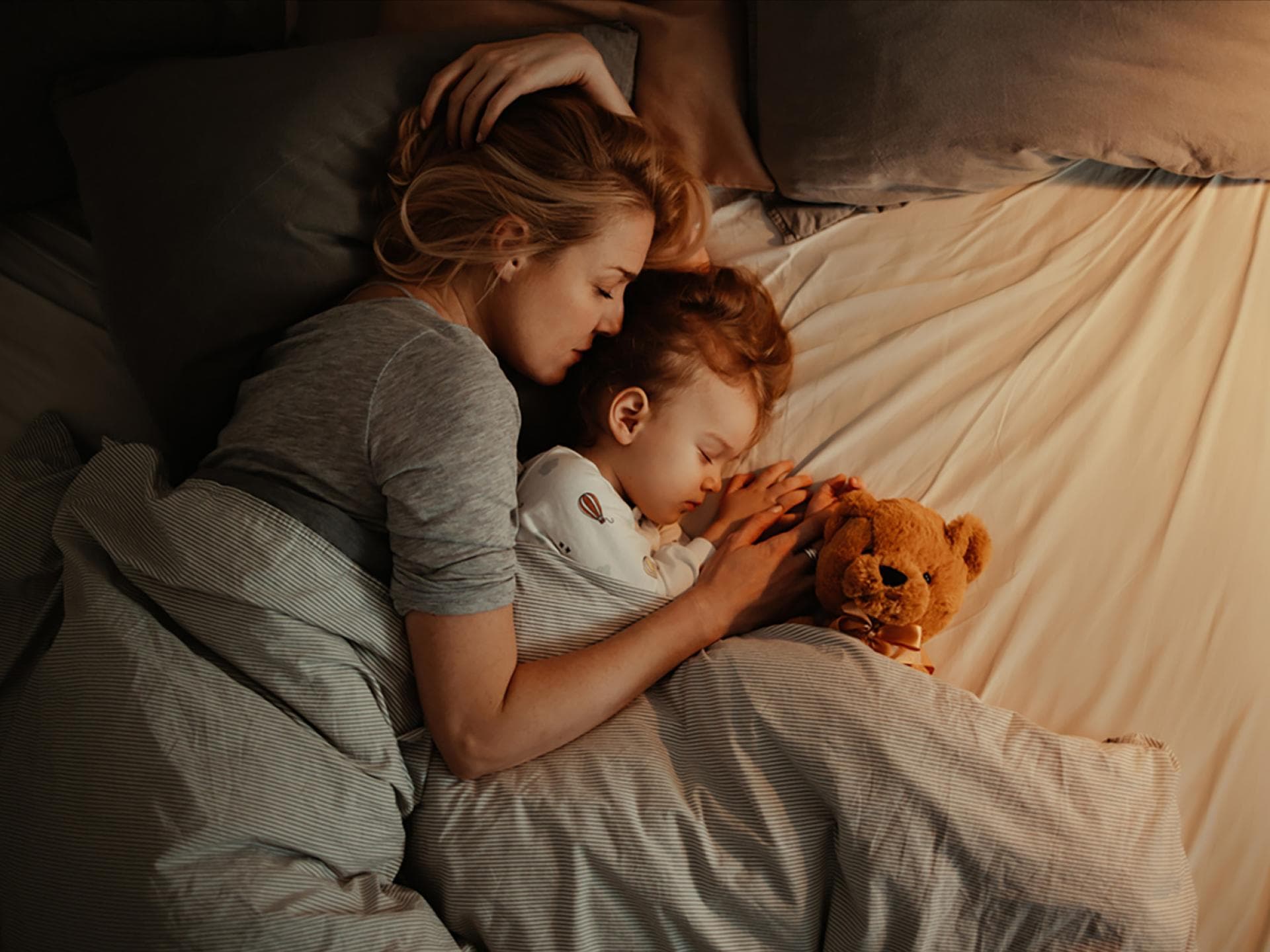 Das Baby schläft nicht alleine? Einschlafroutinen können dabei helfen, das Alleineschlafen anzugewöhnen. Mutter liegt mit kleinem Kind im Bett.