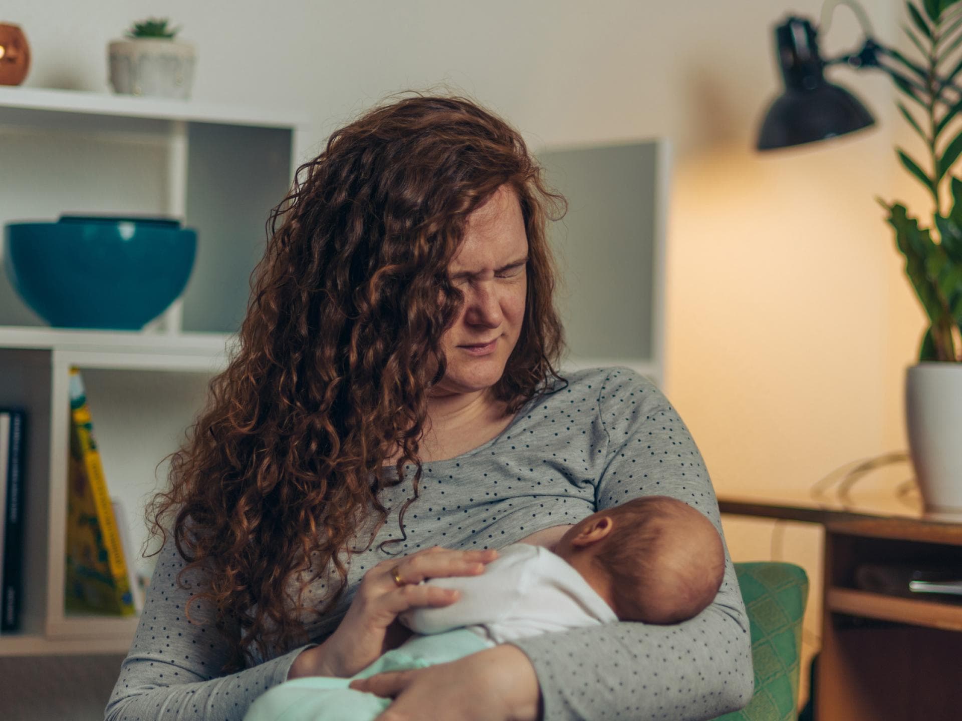 Eine Frau mit Milchstau stillt ihr Baby und beißt dabei die Zähne zusammen. Frau stillt mit schmerzverzerrtem Gesicht ihr Baby.