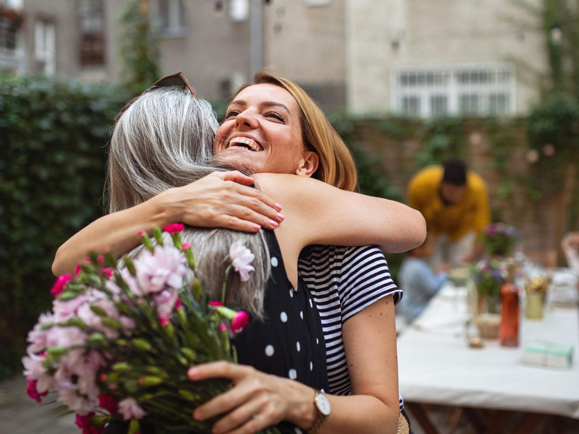 Erwachsene Frau umarmt ihre Mutter mit Blumen.