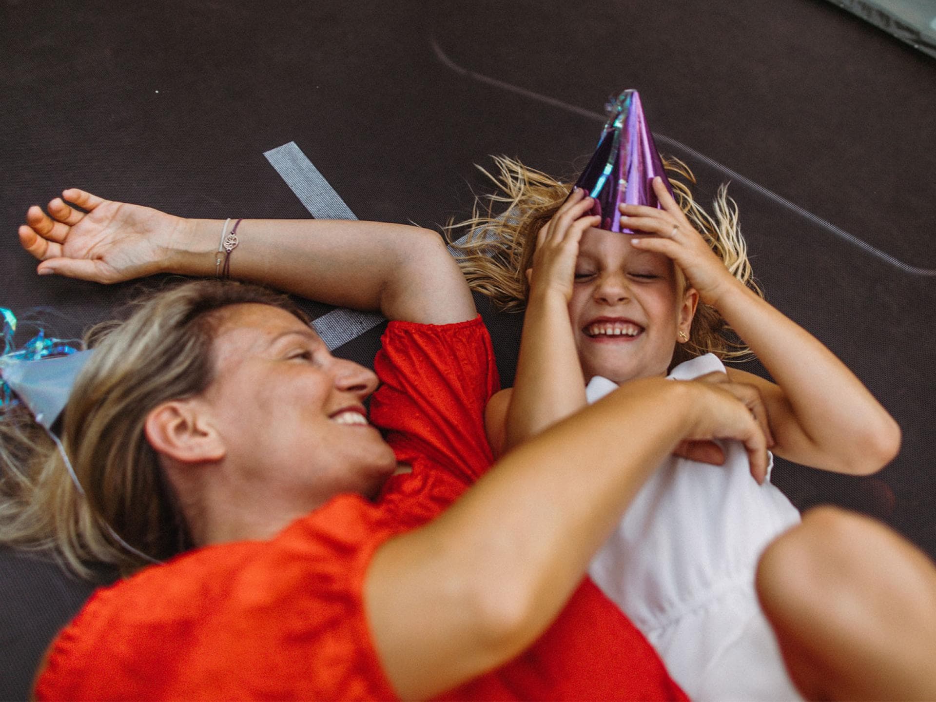 Ab aufs Trampolin: Mit Kind kann man endlich wieder die lustigen Dinge von früher machen! Mutter und Kind liegen auf Trampolin.