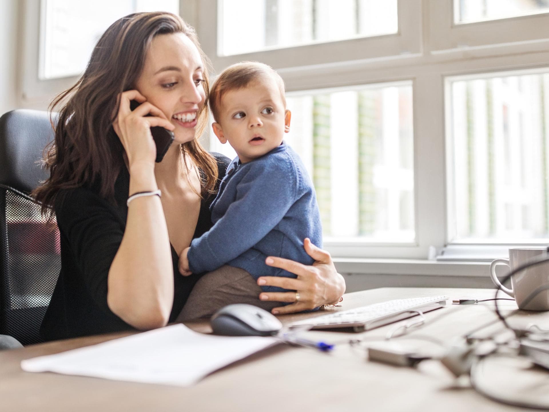 Mutter arbeitet mit Kind auf dem Schoß.