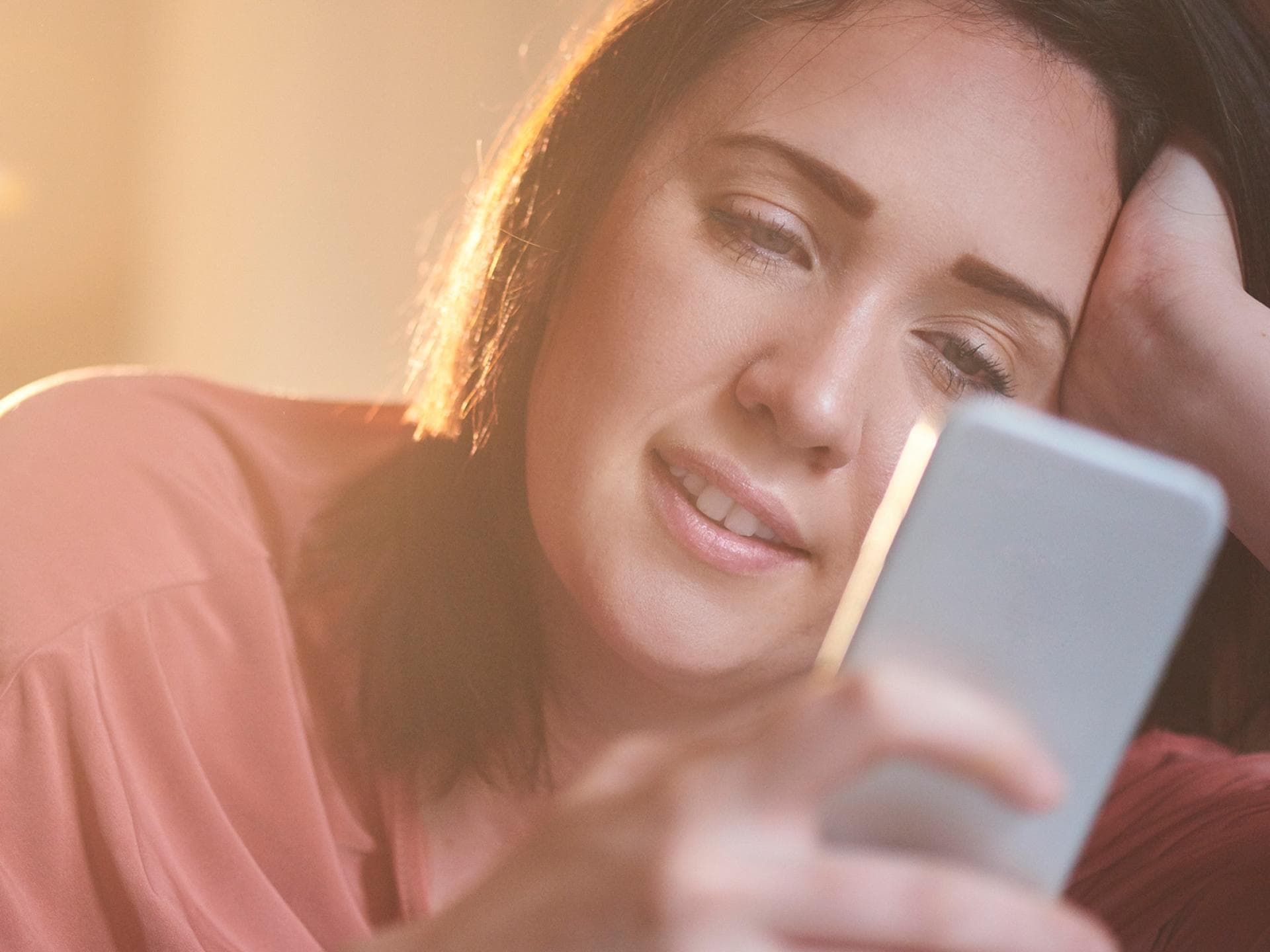 Frau lächelt, während sie auf ihr Smartphone schaut.