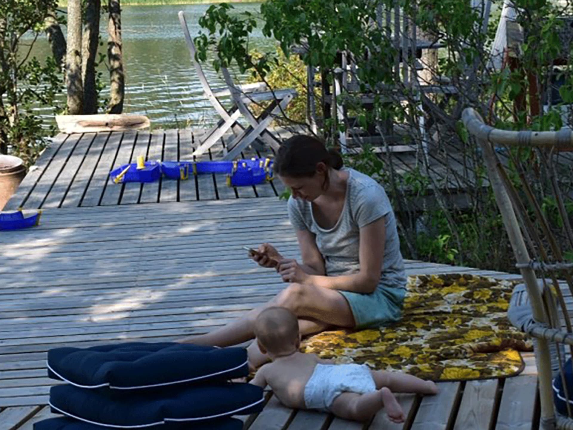 Mutter mit Baby am Wasser mit Handy in der Hand.