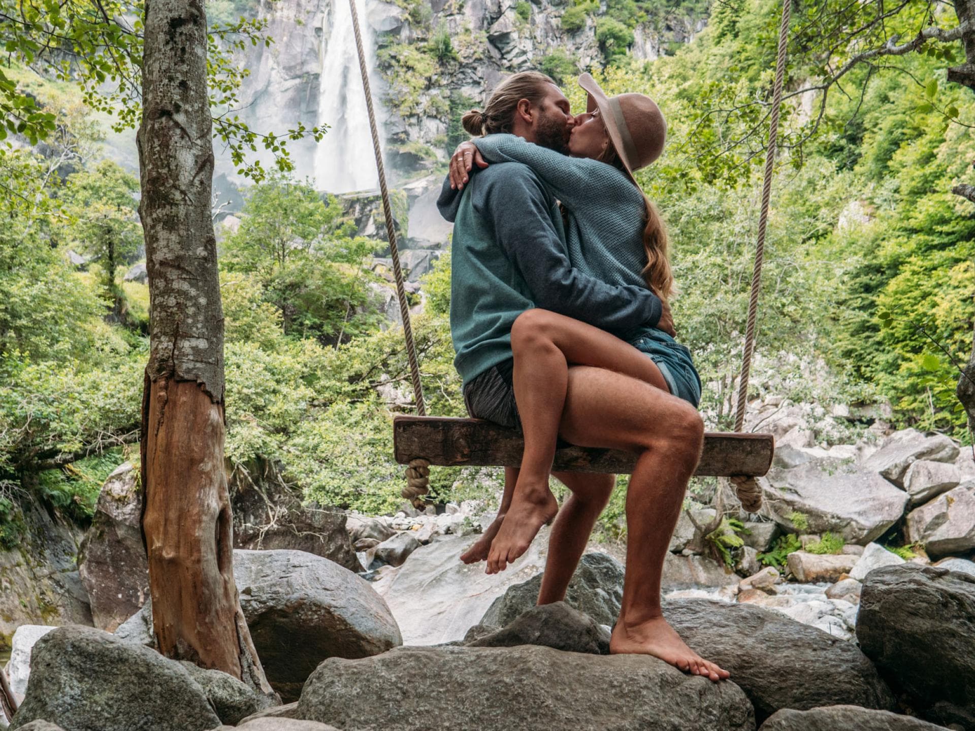 Paar sitzt sich küssend auf einer Schaukel in der Natur.