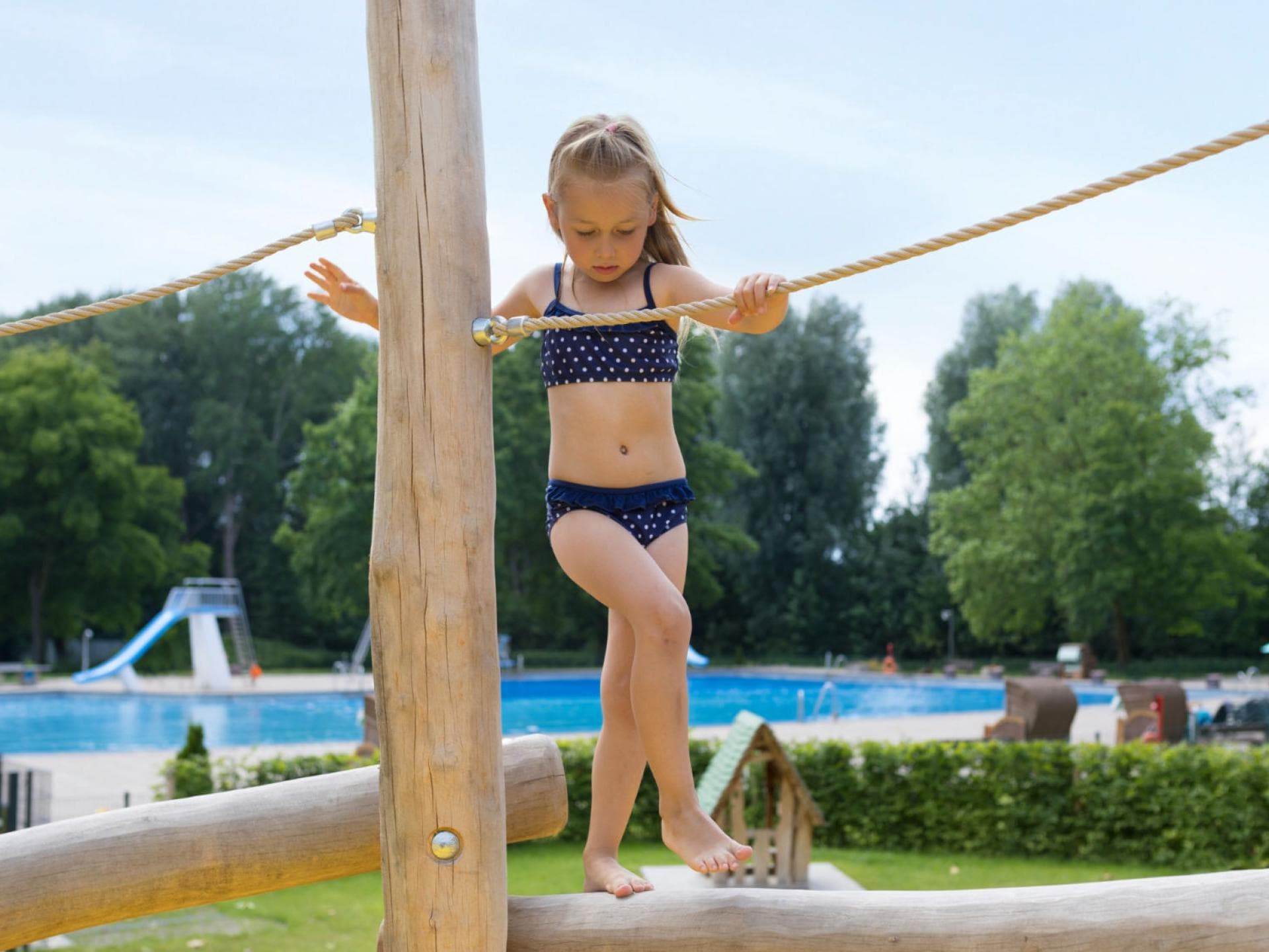 Im Badeurlaub mit Kindern heißt es für die Eltern: immer gut aufpassen. Mädchen balanciert im Schwimmbad.