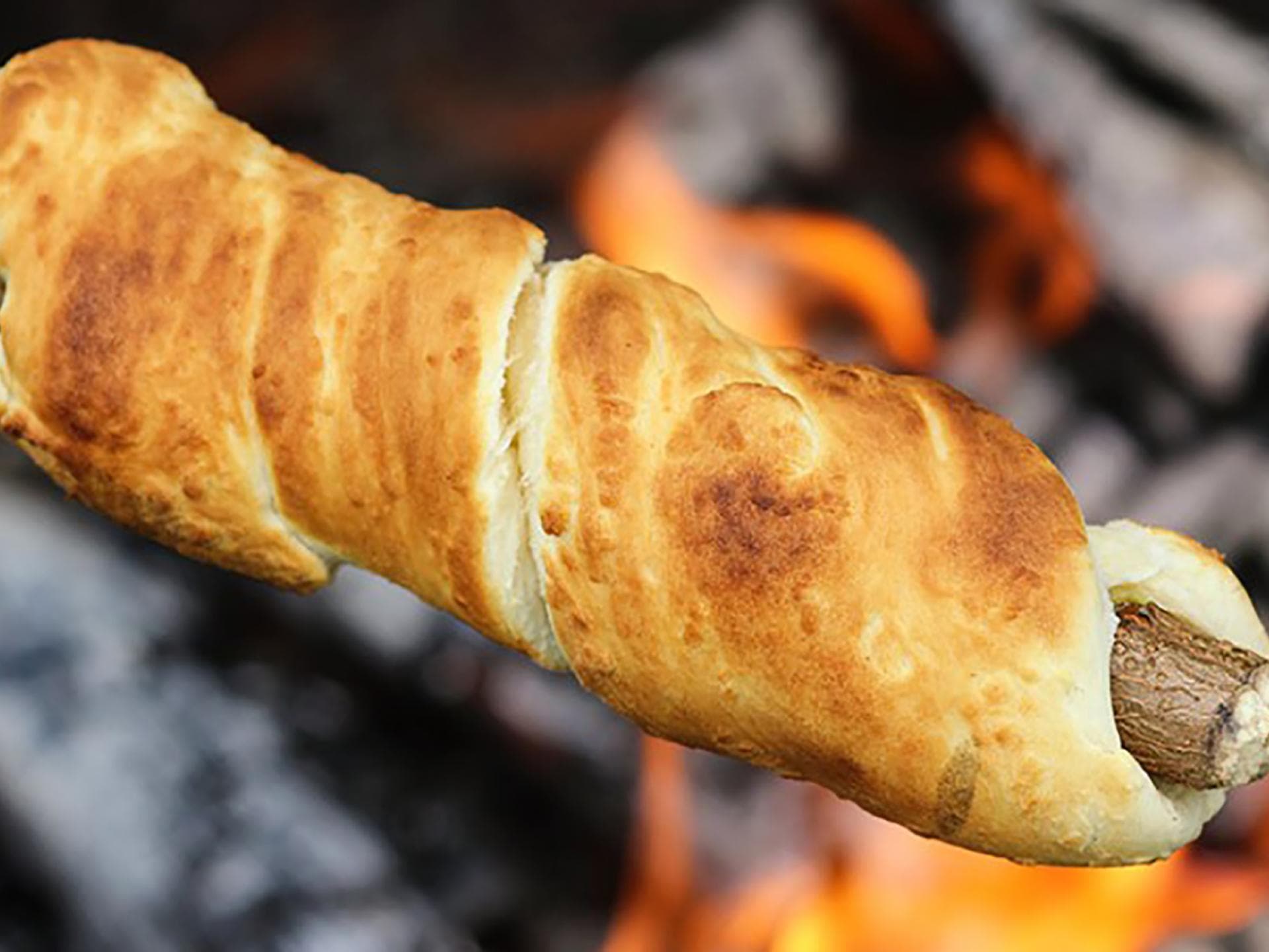 Ein Stockbrot aus Pizzateig wird am Lagerfeuer gegrillt. 