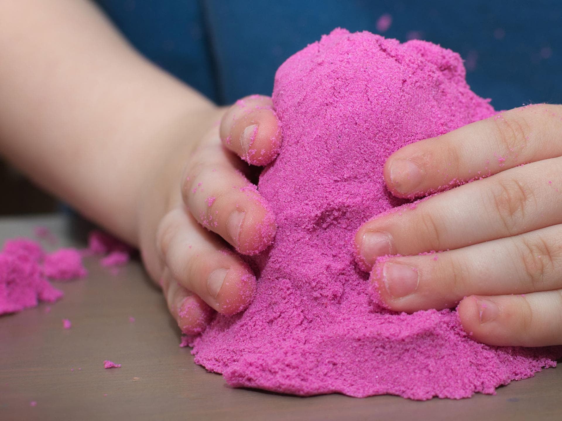 Mit ein wenig Lebensmittelfarbe wird der Kinetic Sand (Zaubersand) noch schöner. Kinderhände mit pinkfarbenem Kinetic Sand.