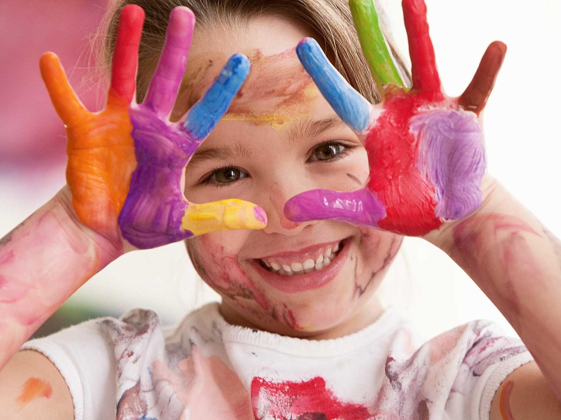 Fröhliches Kind mit bunten Fingerfarben an den Händen.