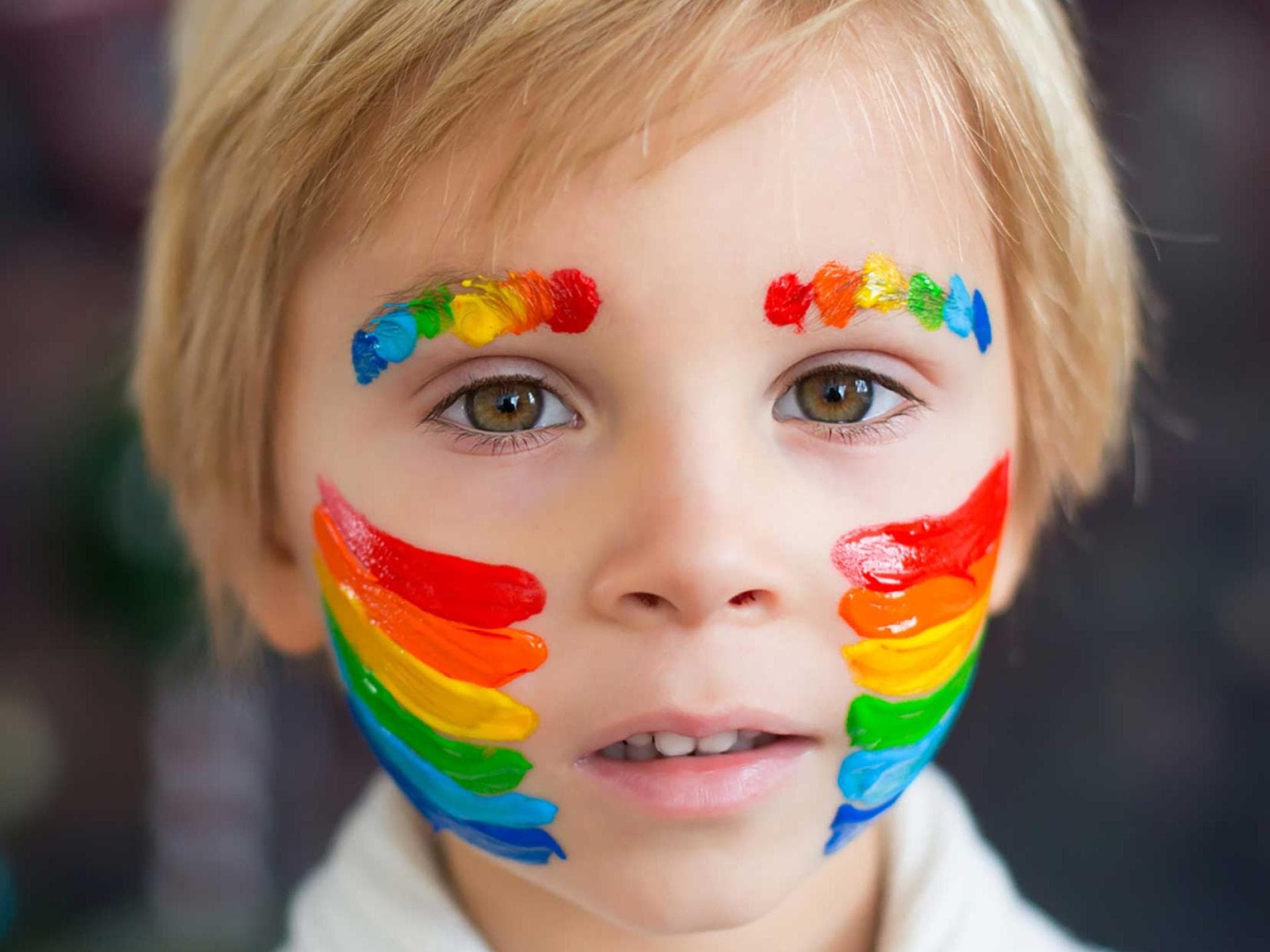 Junge mit geschminktem Regenbogen auf Wangen und Augenbrauen