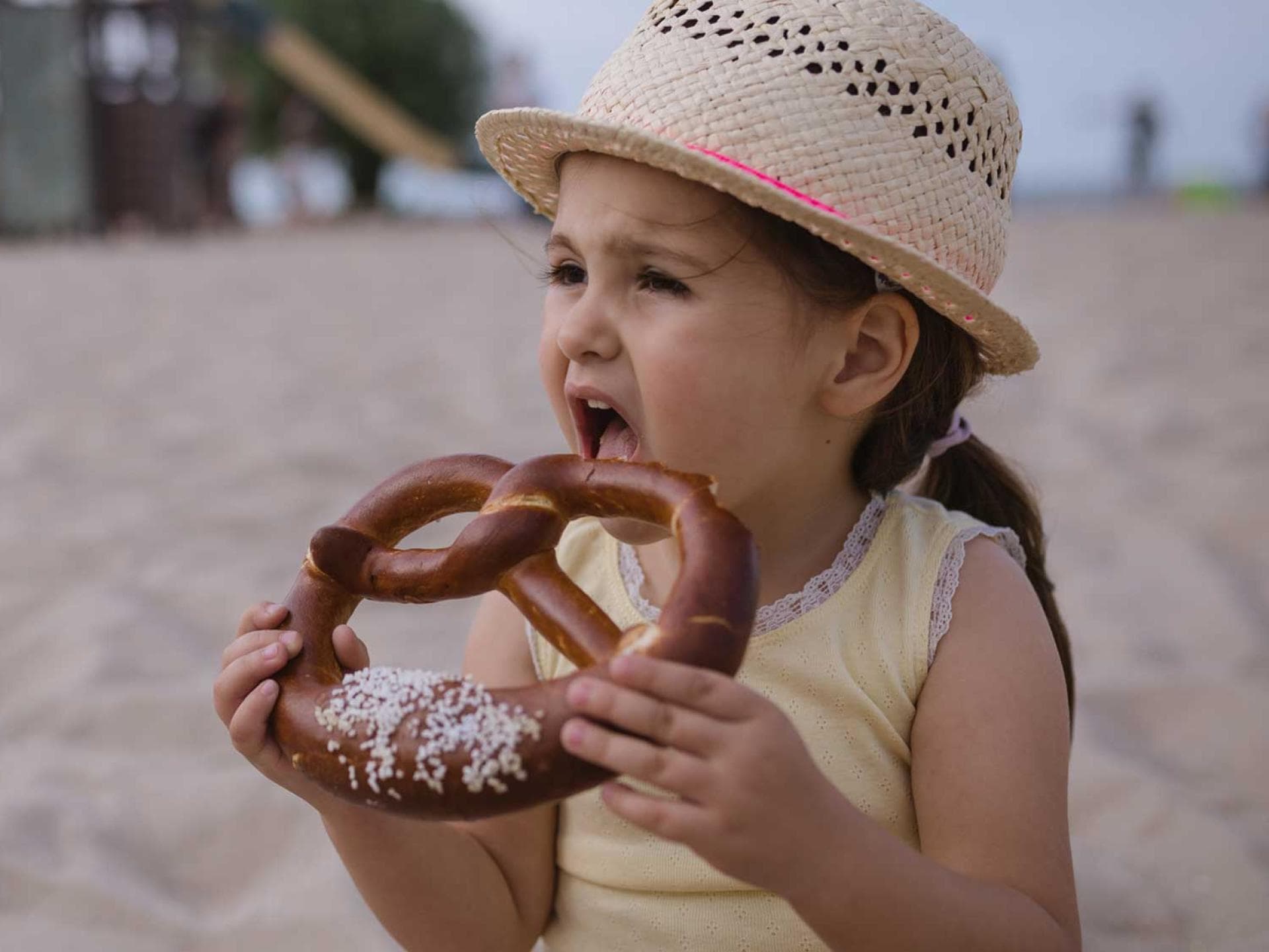 Laugengebäck enthält selbst ohne das aufgestreute Hagelsalz schon ein Gramm Salz. Die Tageshöchstmenge für Babys. Mädchen beißt in eine Laugenbrezel mit viel Salz.