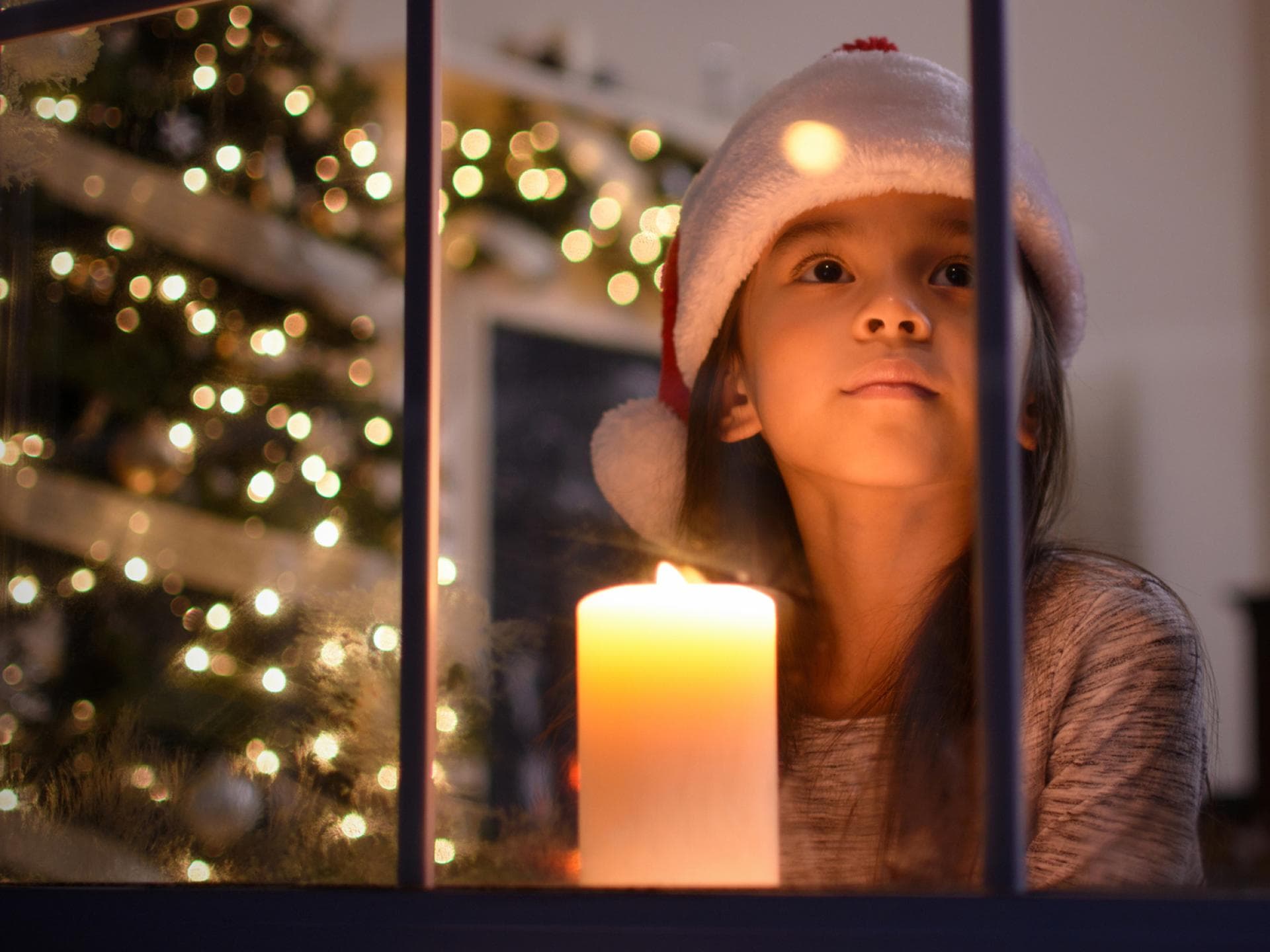 Ein Mädchen schaut aus einem weihnachtlichen Fenster.