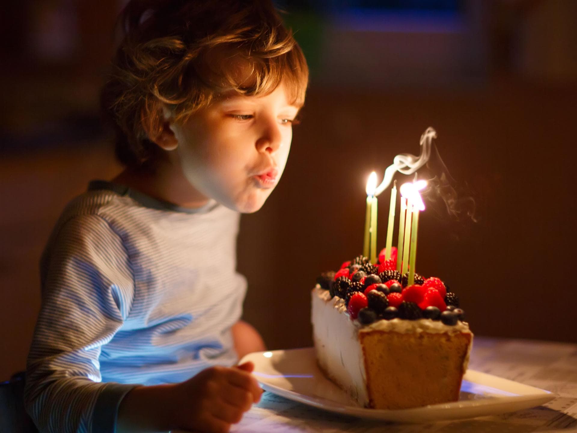 Rituale stärken Kinder.  Kind pustet Kerzen auf Geburtstagskuchen aus.