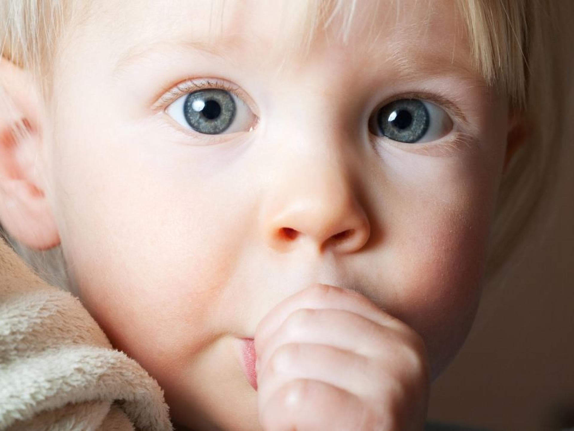 Kleines Kind nuckelt mit großen Augen am Daumen.