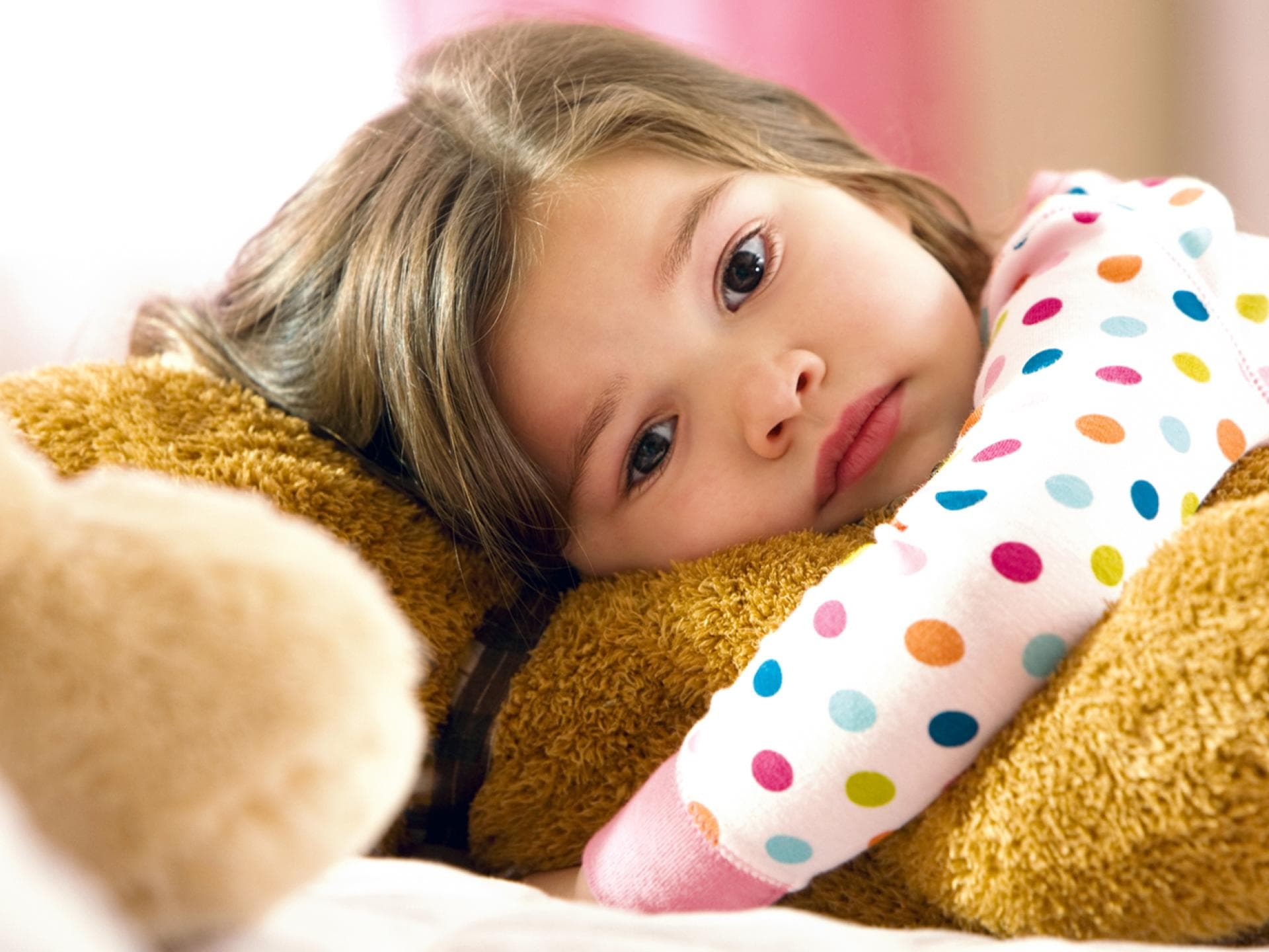 Mit Enttäuschungen klarzukommen, ist für kleine Kinder nicht immer leicht. Ein kleines Mädchen schmollt mit seinem Teddy auf dem Bett.