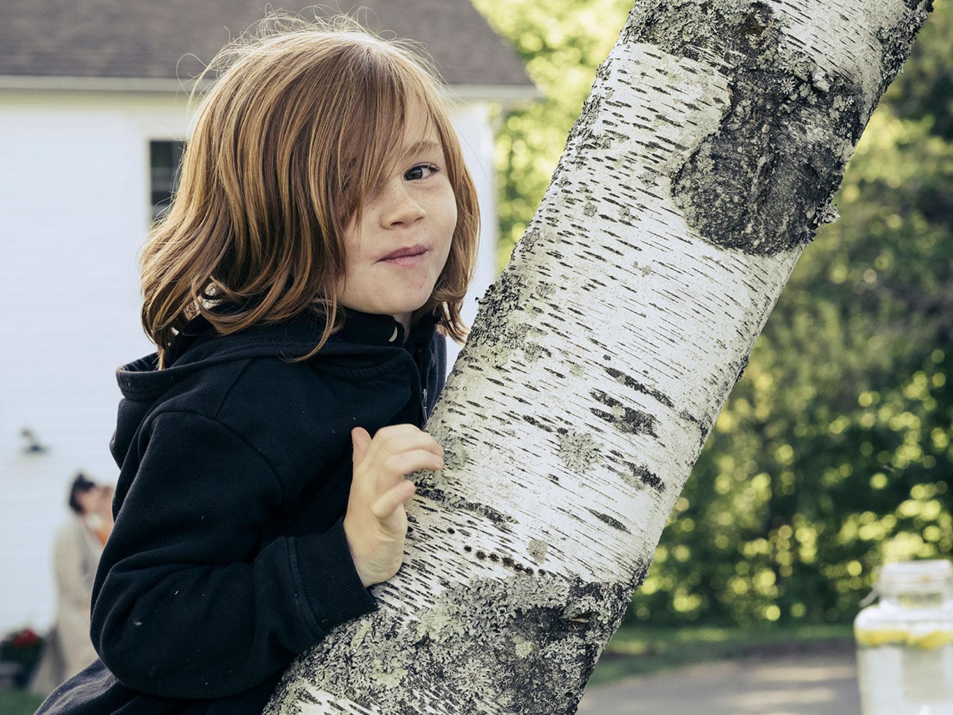 Vielen Jungen stehen lange Haare ziemlich gut. Junge mit langen Haaren lehnt an einer Birke.