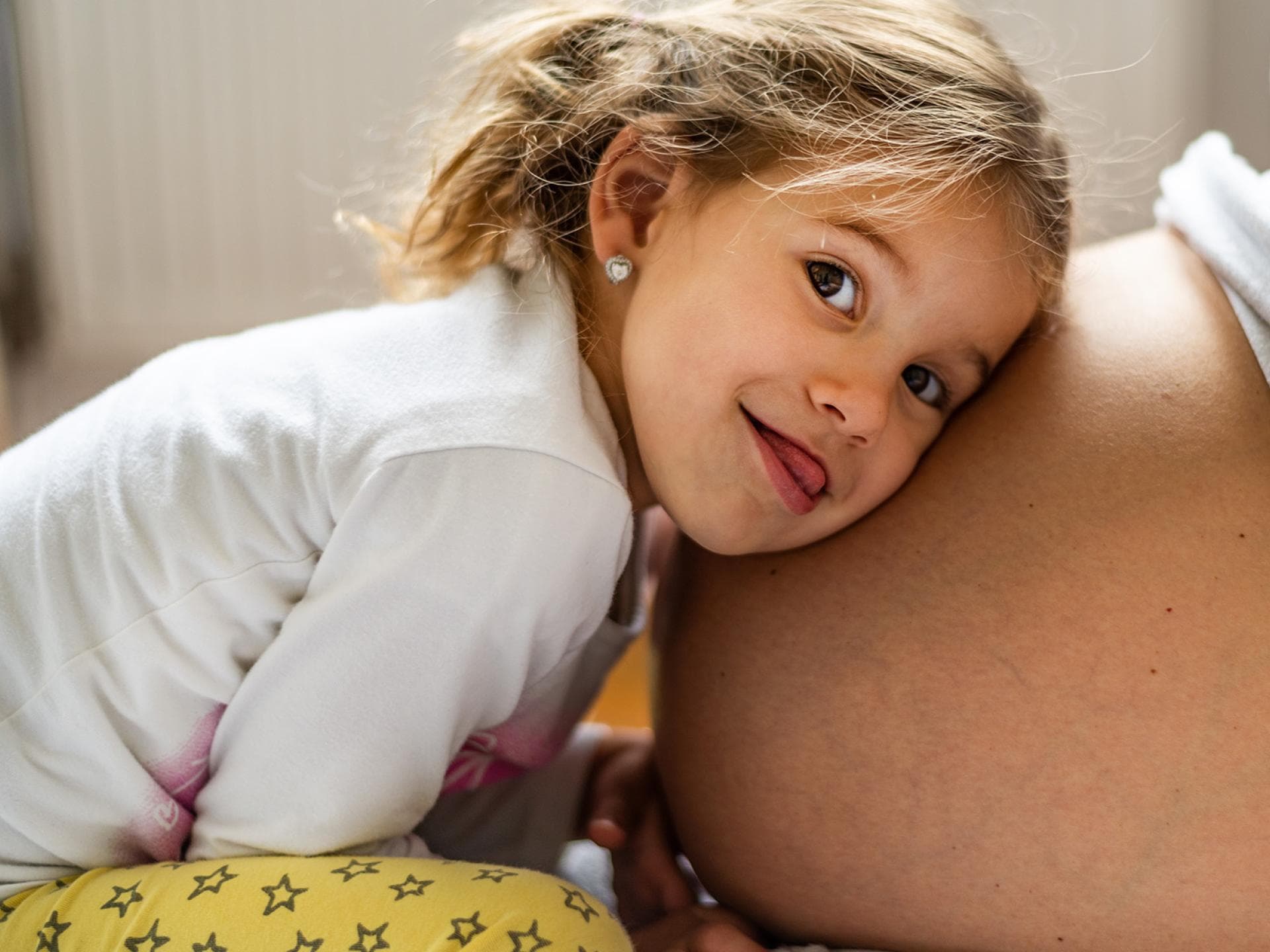 Spannend, wenn in Mamas Bauch ein Baby wächst! Fröhliches Mädchen lauscht am Babybauch.