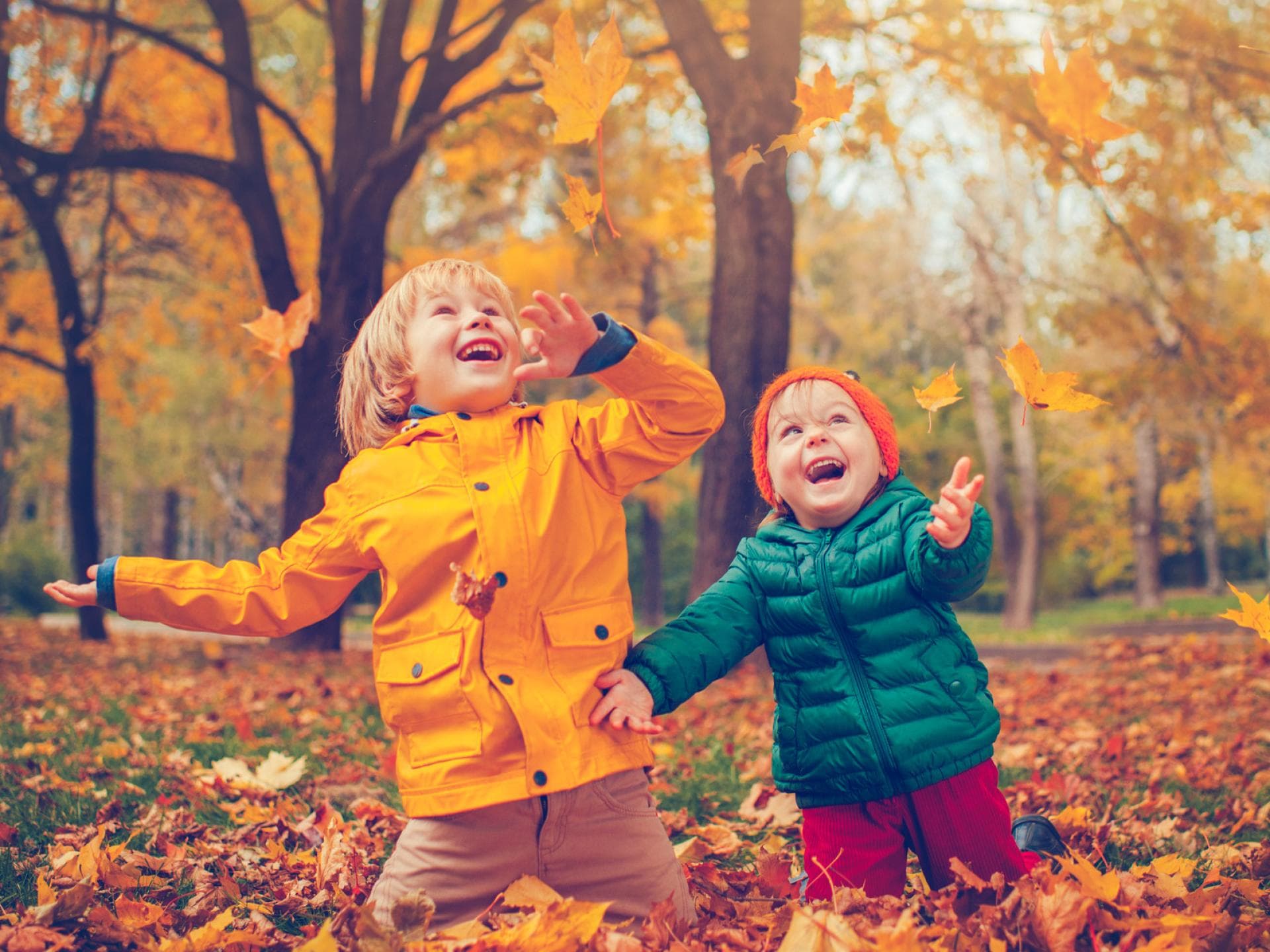 Richtig cool am Herbst: Die vielen bunten Blätter, die zum Spielen einladen ... Zwei Kinder freuen sich über buntes Herbstlaub.