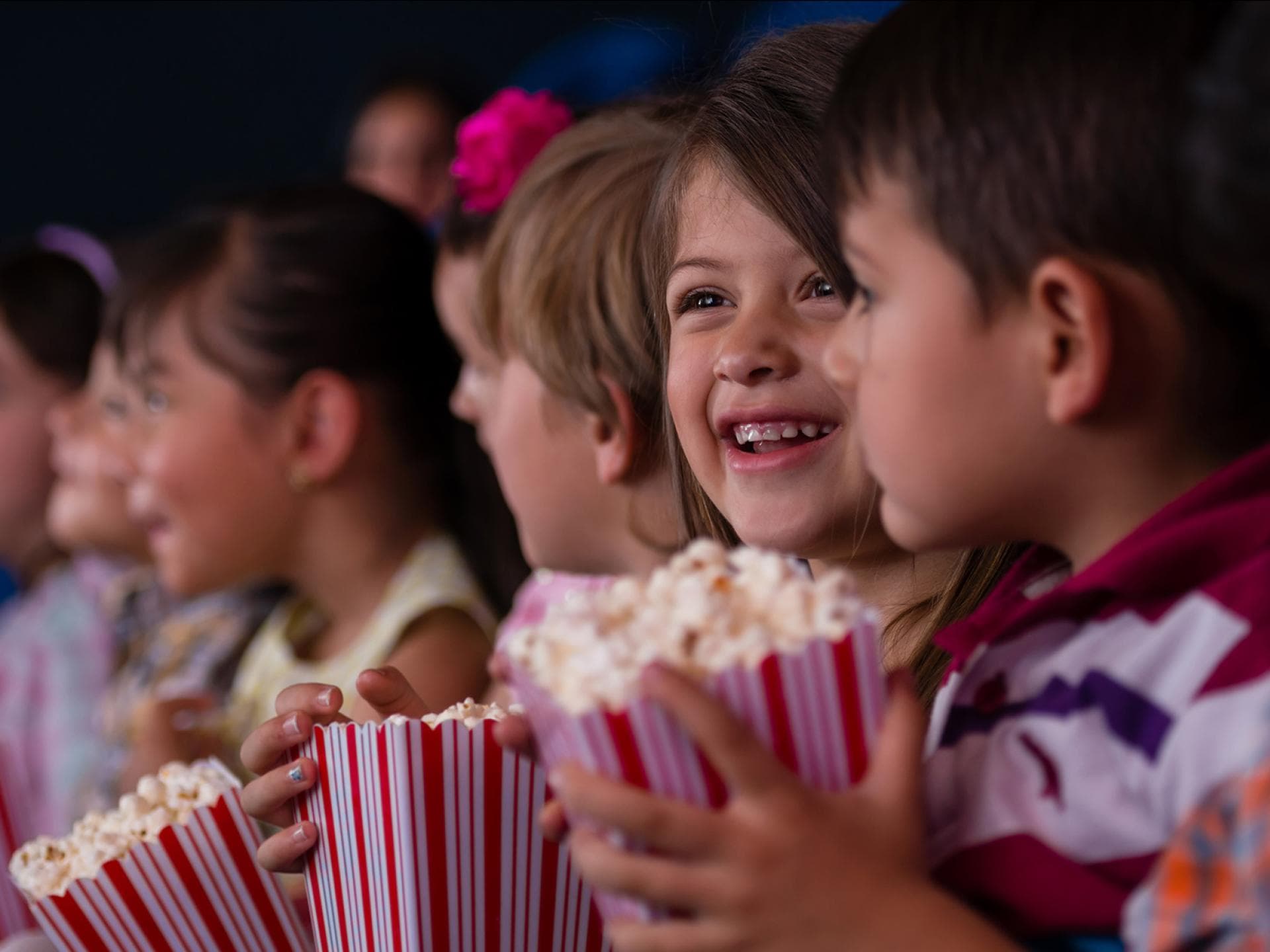 Der erste Ausflug ins Kino oder auch eingekuschelt auf dem Sofa – ein schöner Kinderfilm kann Klein und Groß Spaß machen. Zwei Kinder sitzen im Kino mit einer Tüte Popcorn in der Hand.