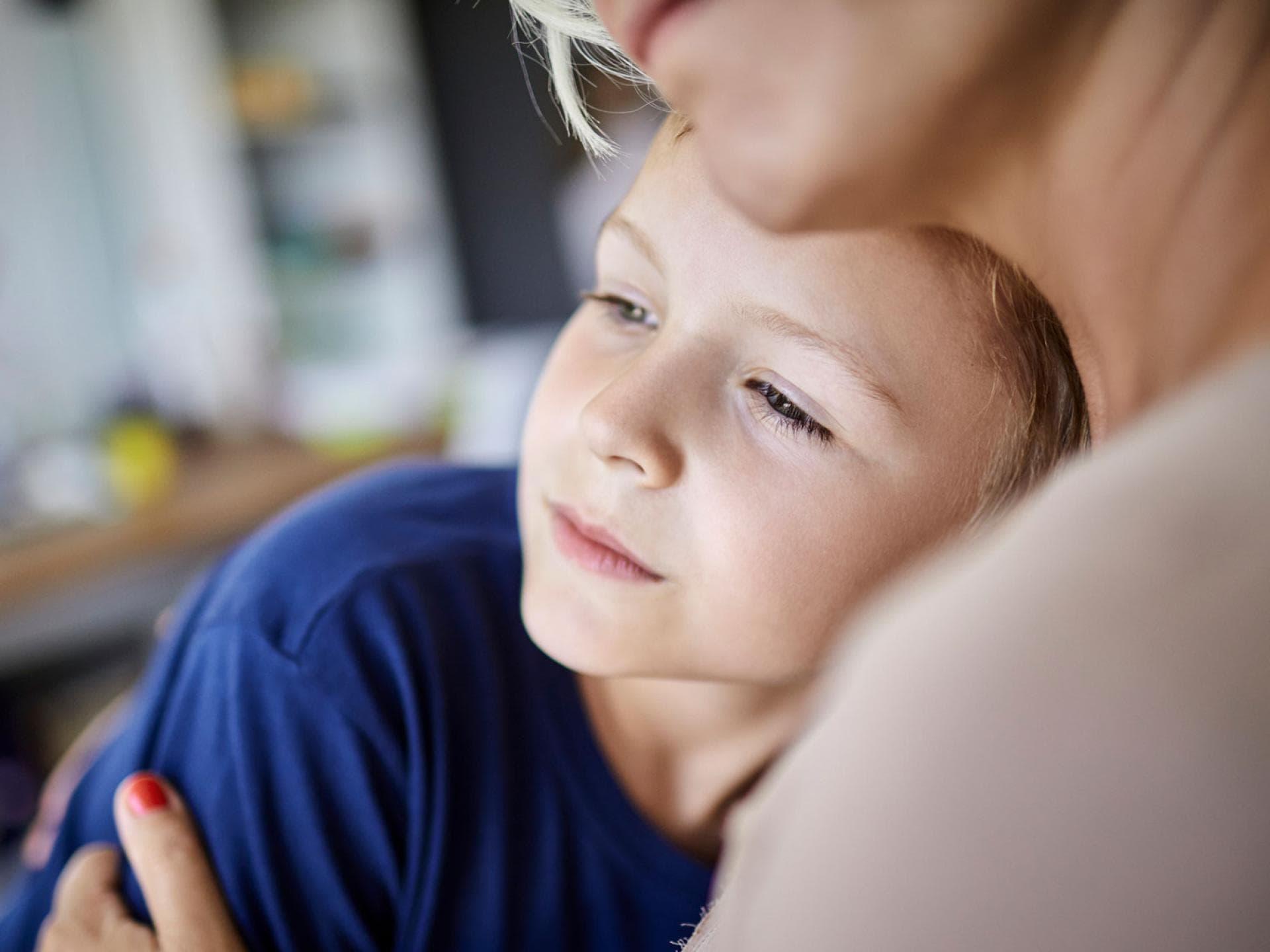 Parentifizierte Kinder ziehen sich manchmal im sozialen Umfeld zurück. Jüngere Kinder klagen mitunter über Bauchschmerzen oder Kopfweh. Ernster Sohn kuschelt mit Mutter.