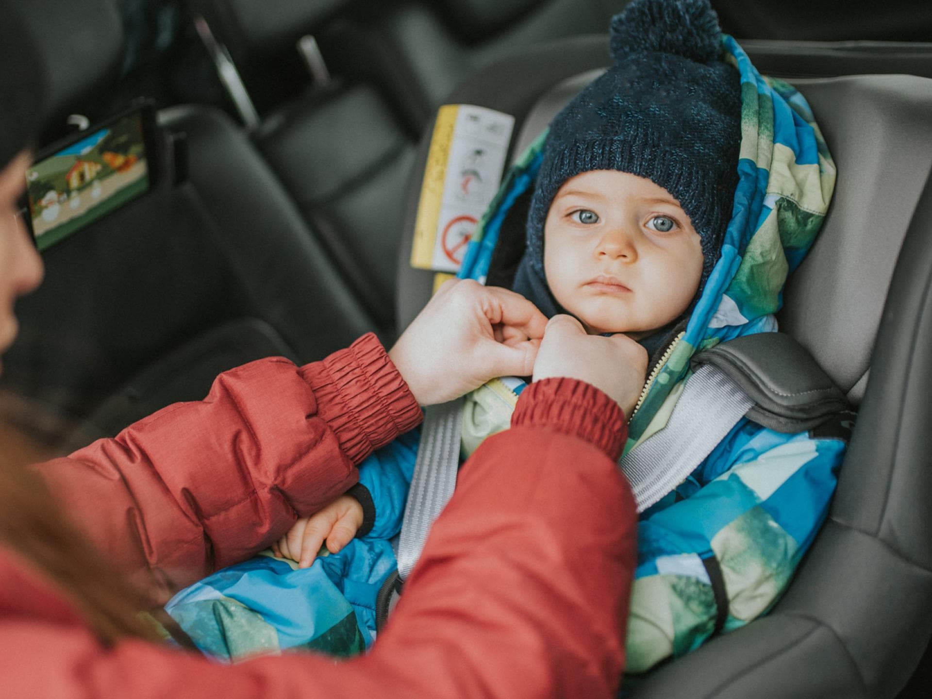 Kinder sollten nicht mit dicker Jacke im Autositz angeschnallt werden. Frau schnallt Baby im Autokindersitz an.