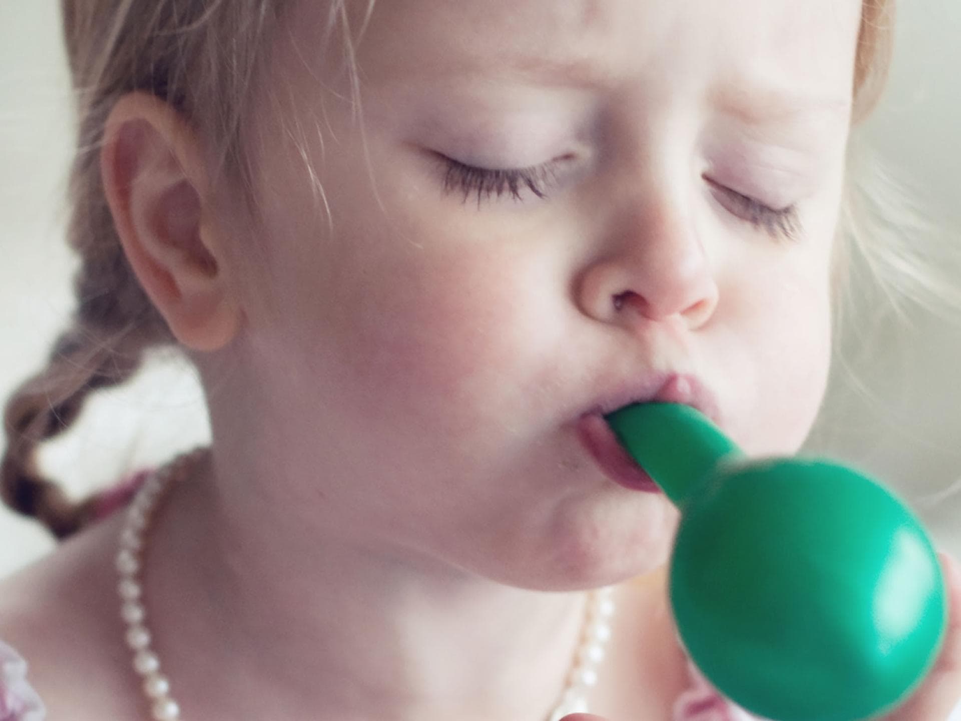 Luftballons können für kleine Kinder tatsächlich gefährlich sein. Mädchen pustet einen Luftballon auf.
