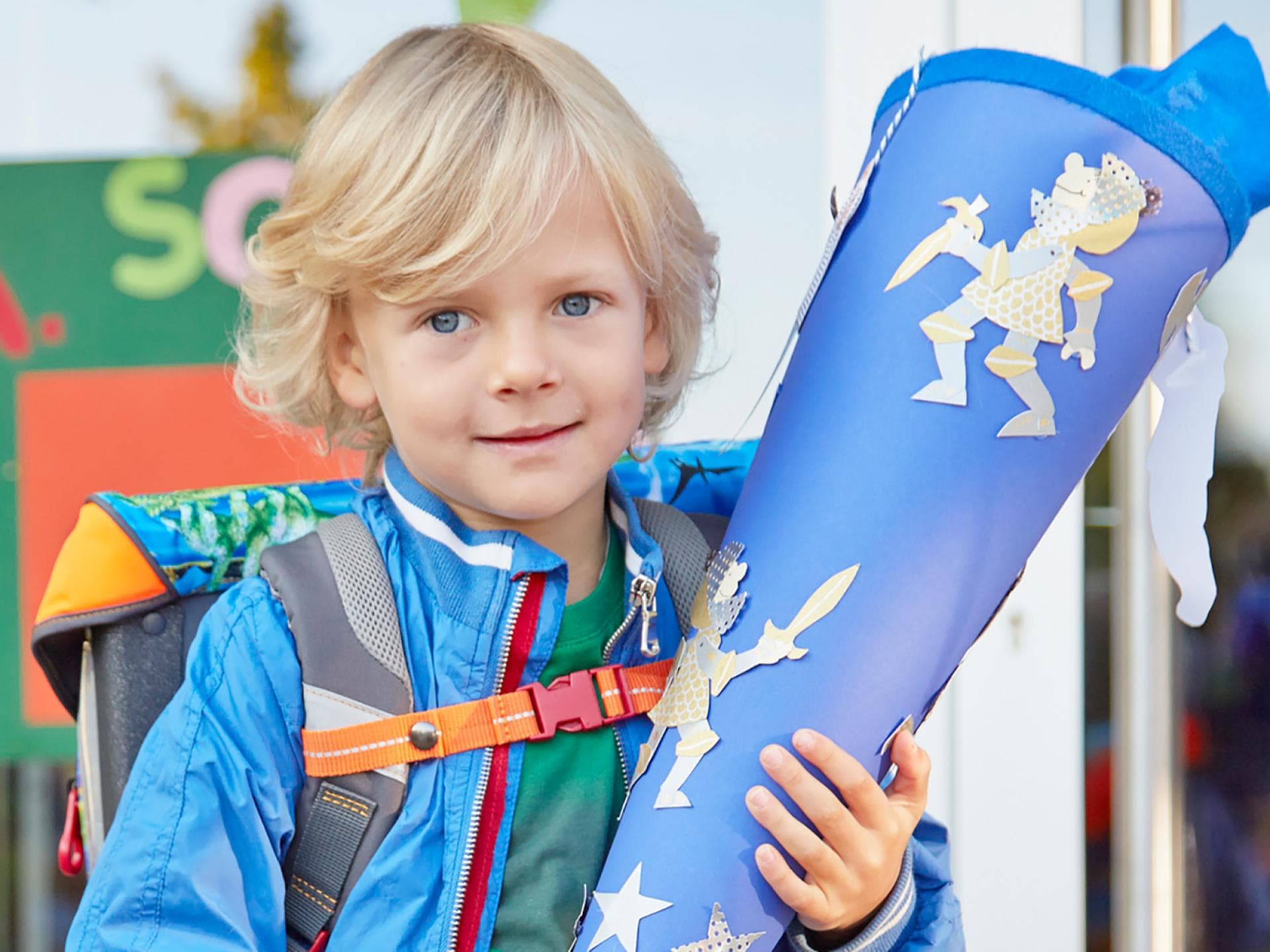 Ein kleiner Junge hat seinen Schulranzen auf und hält stolz seine Schultüte fest.
